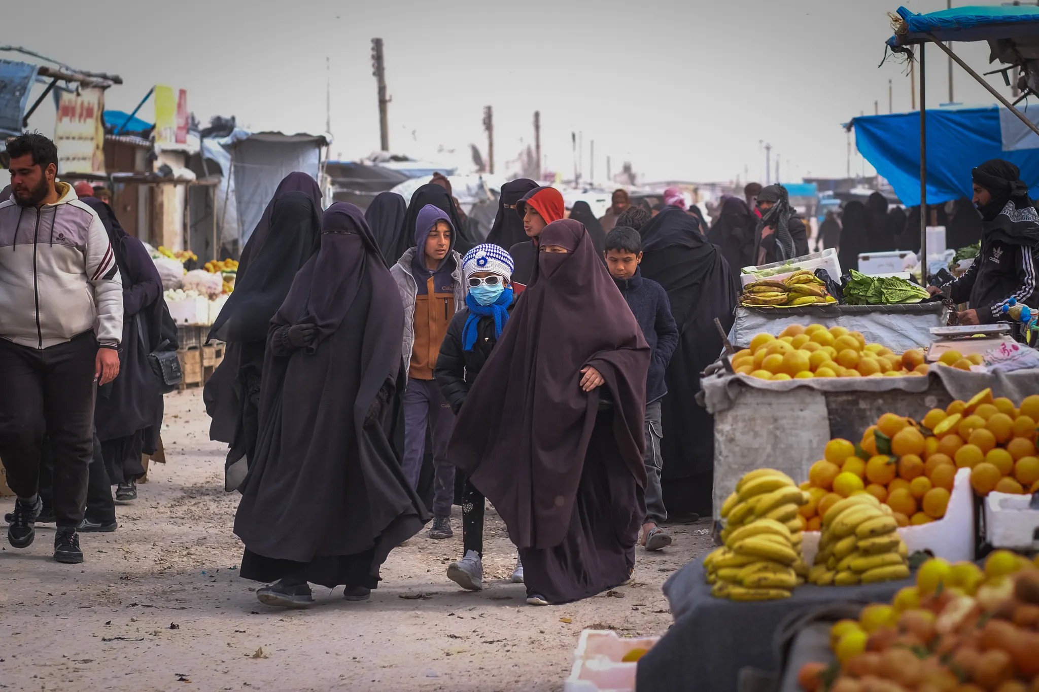 Camp detainees walk through the marketplace in al-Hol