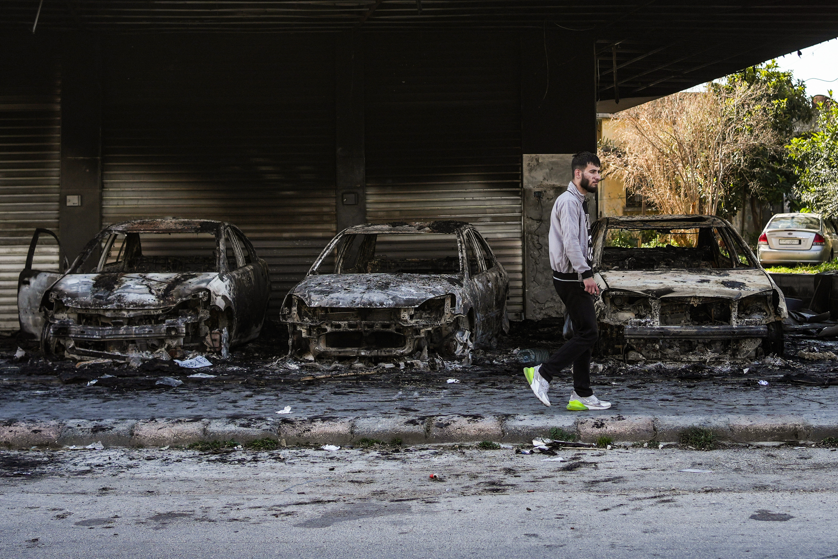 A Syrian man walks past burnt out cars on a street in Jableh town