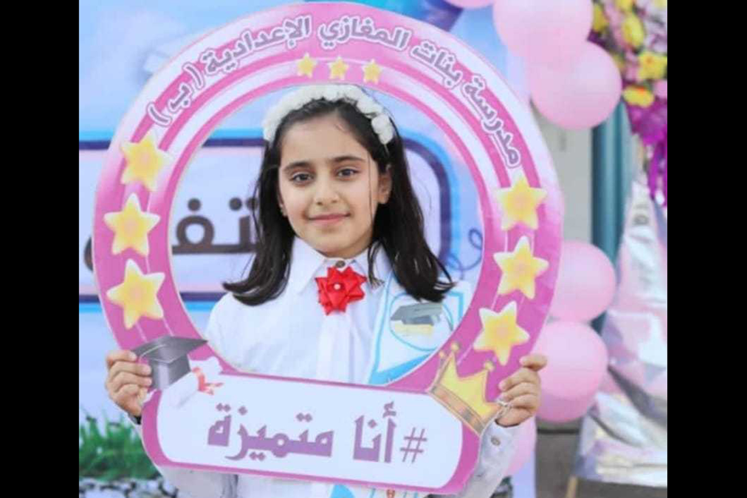 A fifth-grader with dark hair and a white flower headband holds a sign that reads #I_excel