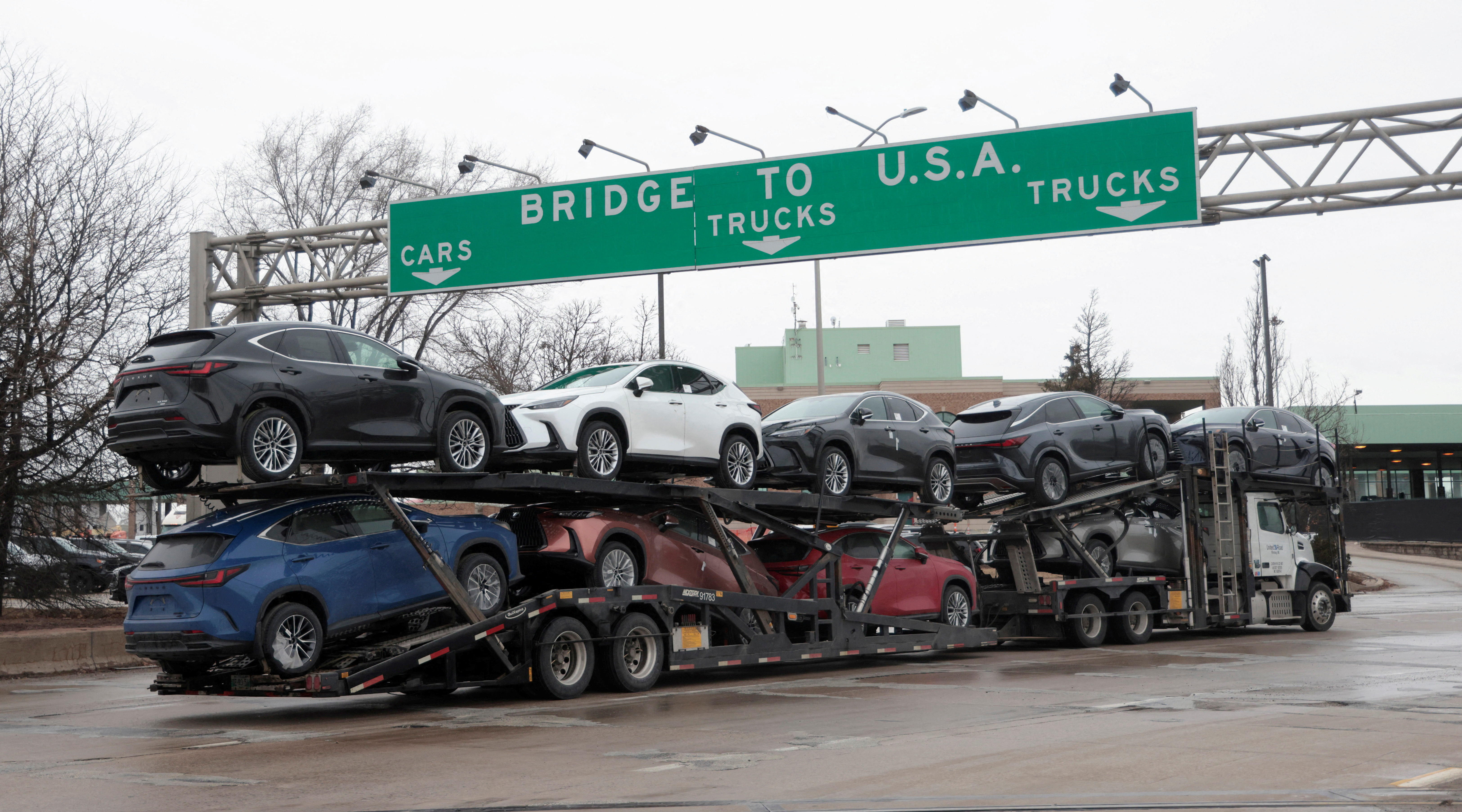 a truck with cars on it drives under a sign that says to the US