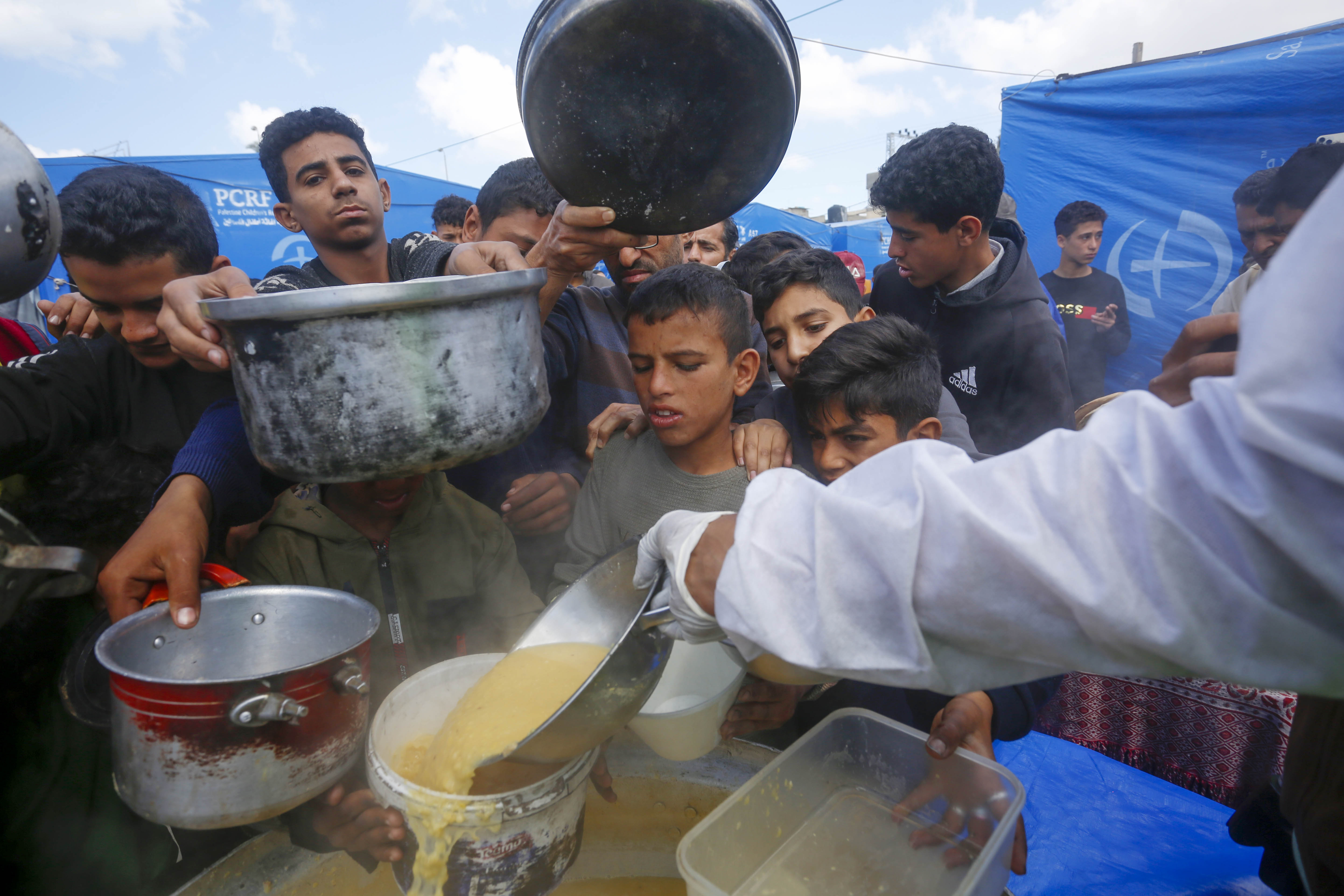 Palestinians, including children, line up to receive hot meals distributed by charities.