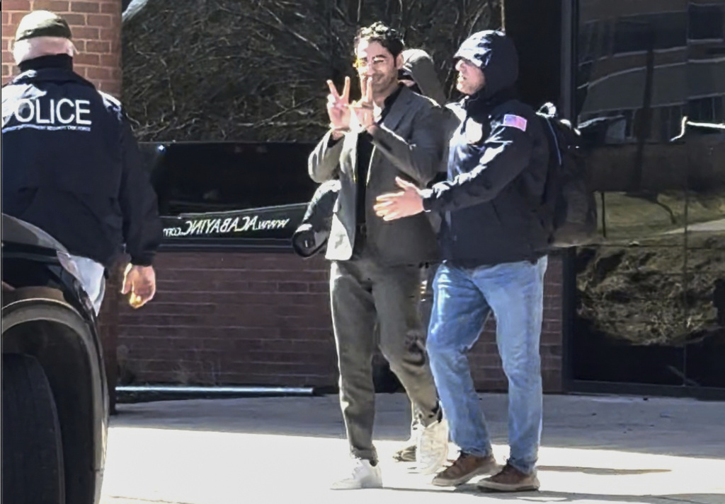 Mohsen Mahdawi makes a victory sign as he is being detained.