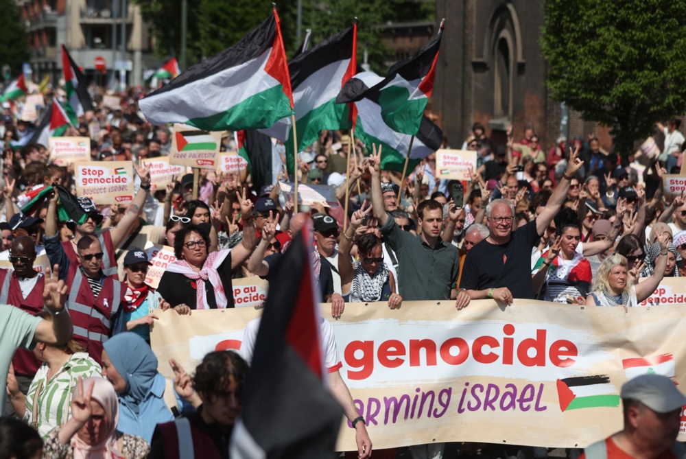 people hold palestinian flags at a protest outside on a street on a sunny day