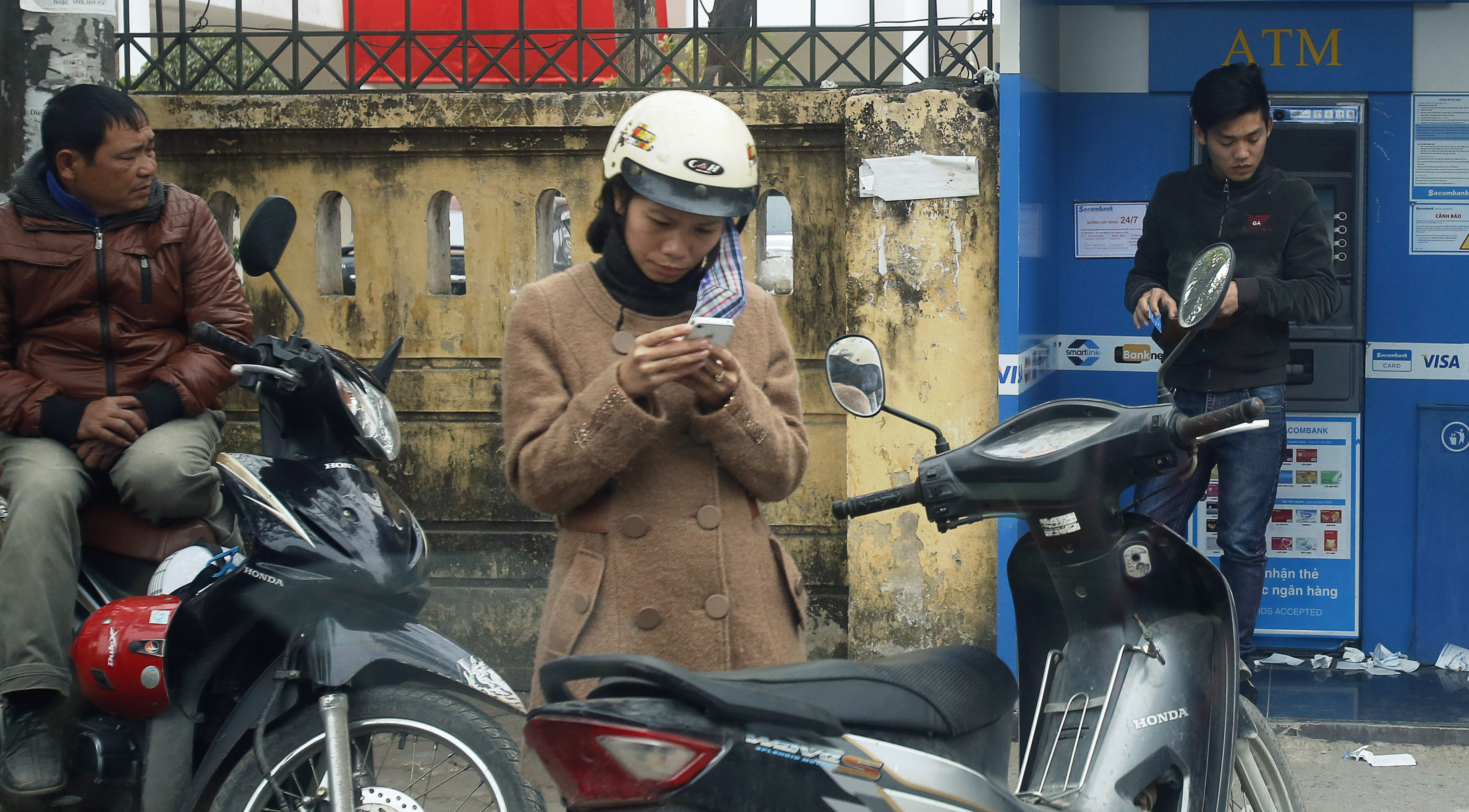 A woman (C) types on a mobile phone along a street in Hanoi February 2, 2015. Vietnam is ringing in changes next month to make way for a standardized phone numbering plan, but is struggling to get through to businesses hung up on how much it will cost them. REUTERS/Kham (VIETNAM - Tags: BUSINESS TELECOMS)