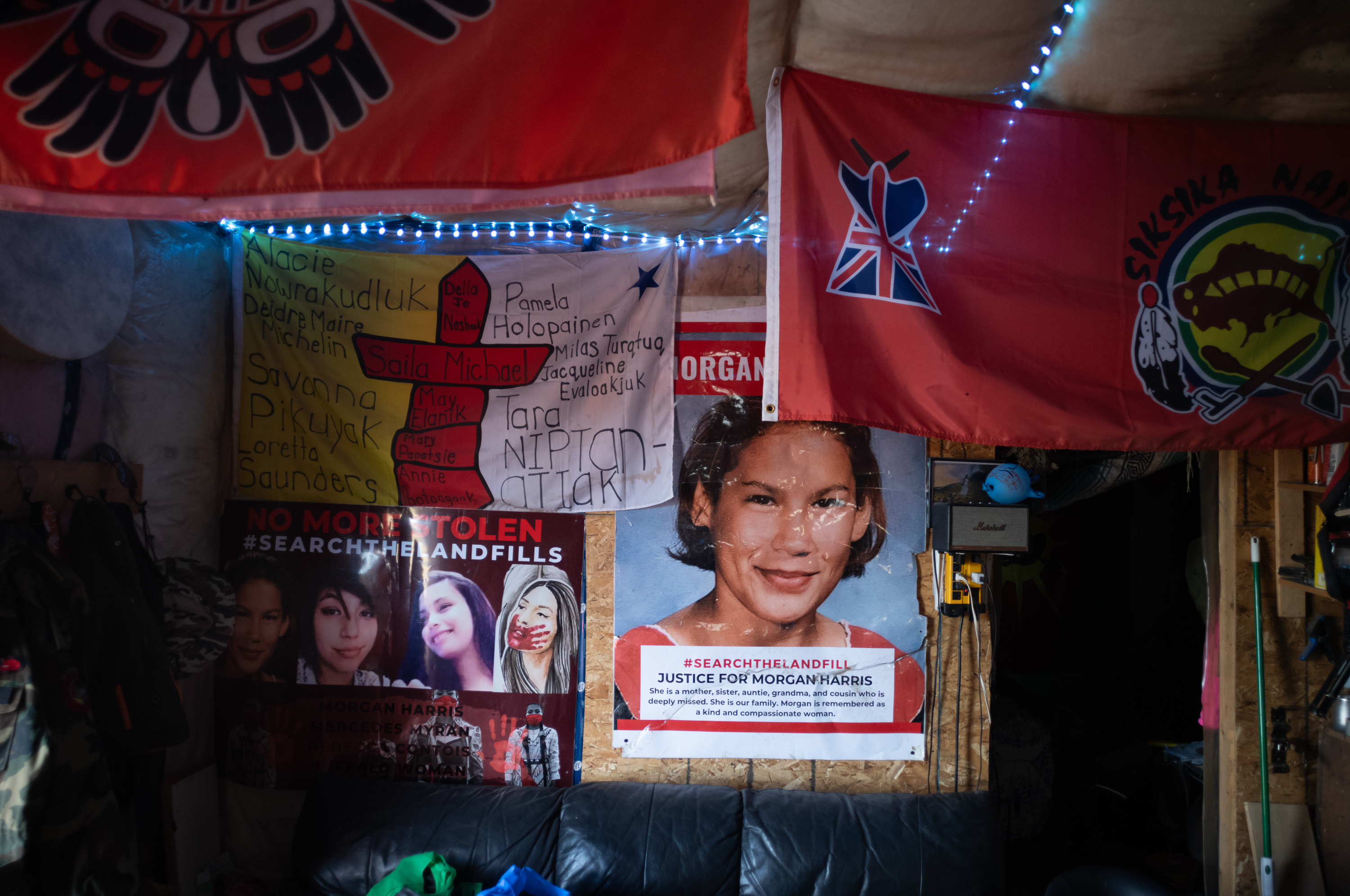 Posters of murdered Indigenous women and girls can be seen on a wooden wall alongside red flags
