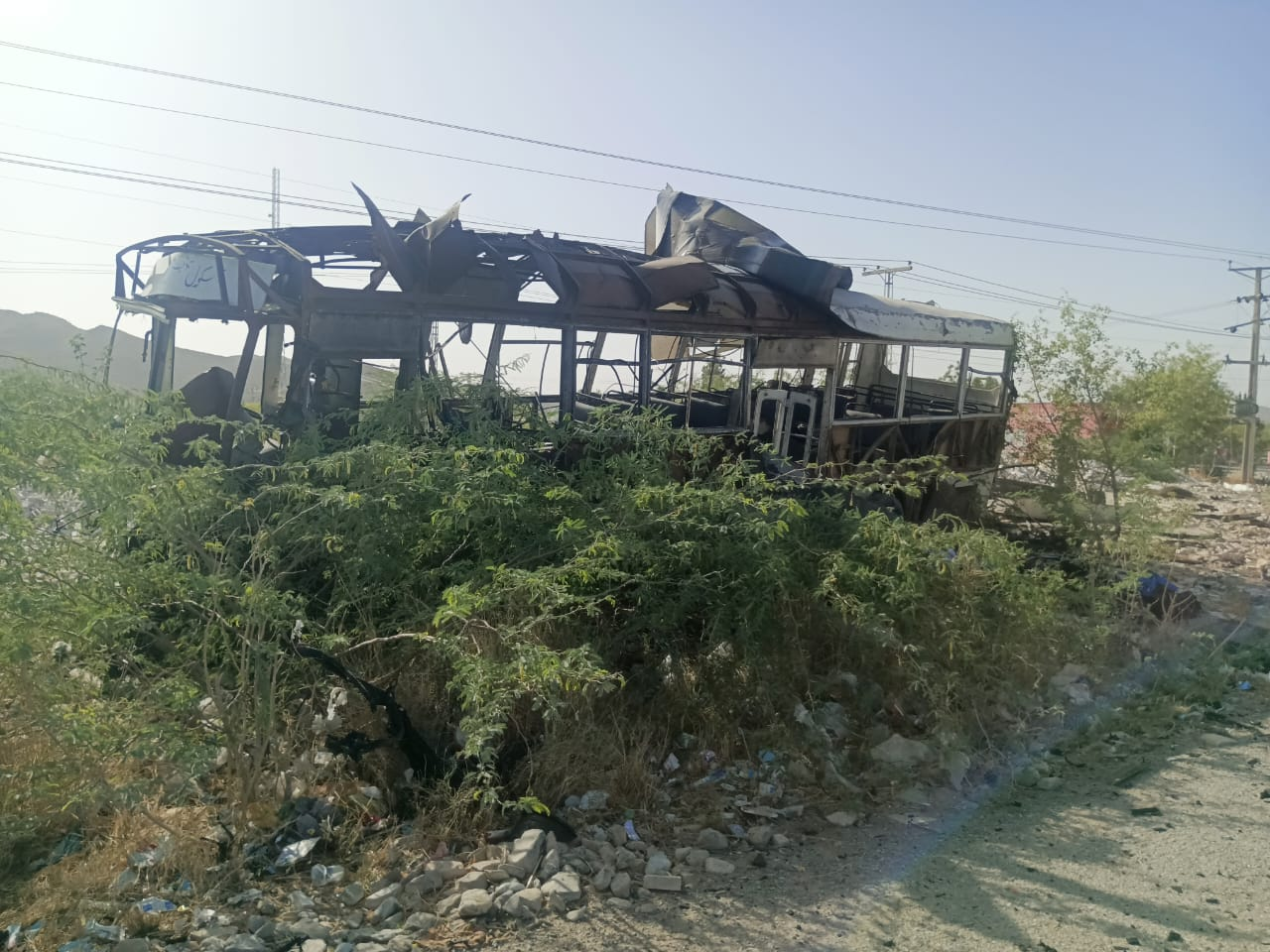 A burned-out bus by a roadside.