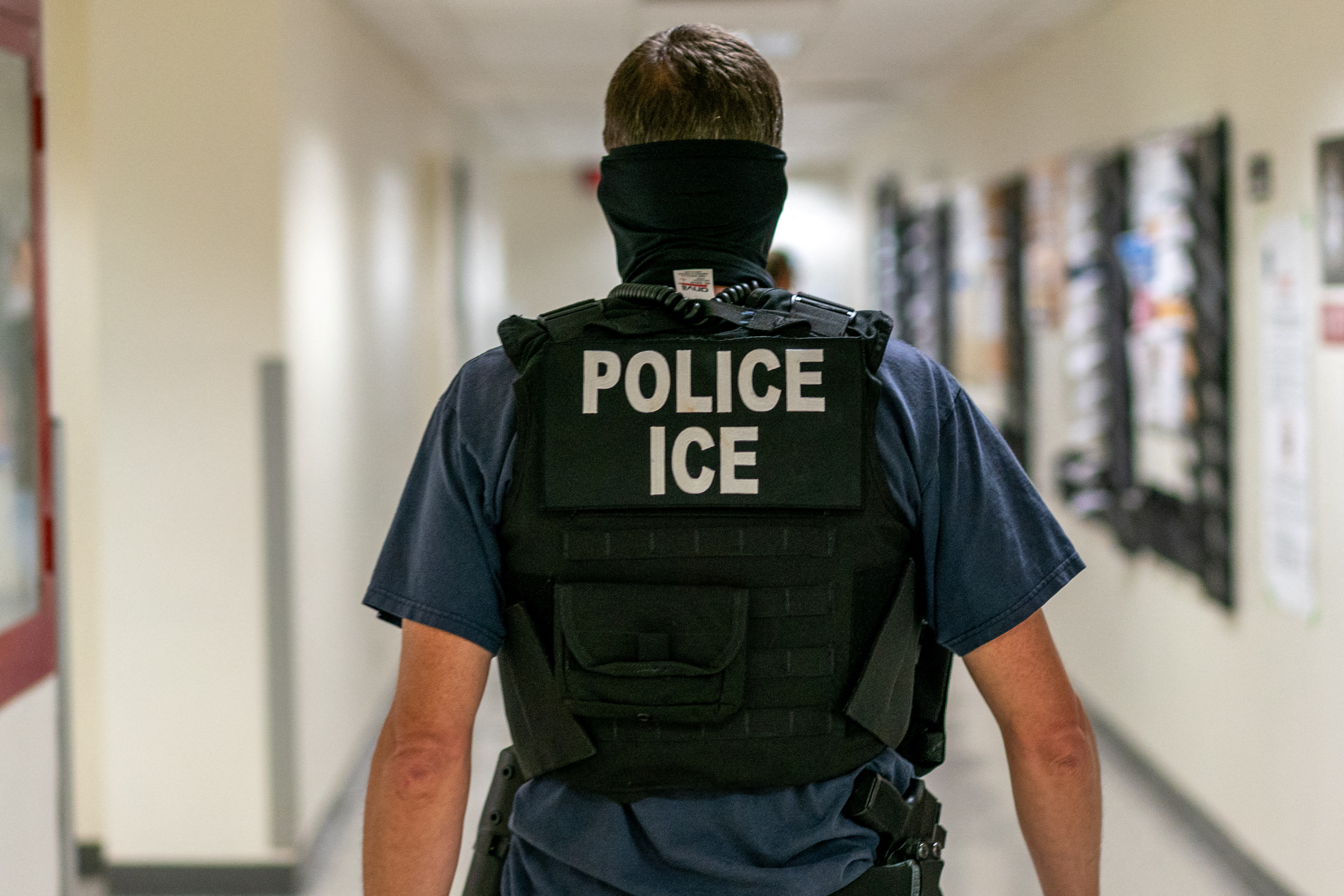 A man wears a bulletproof vest that reads, "POLICE ICE"