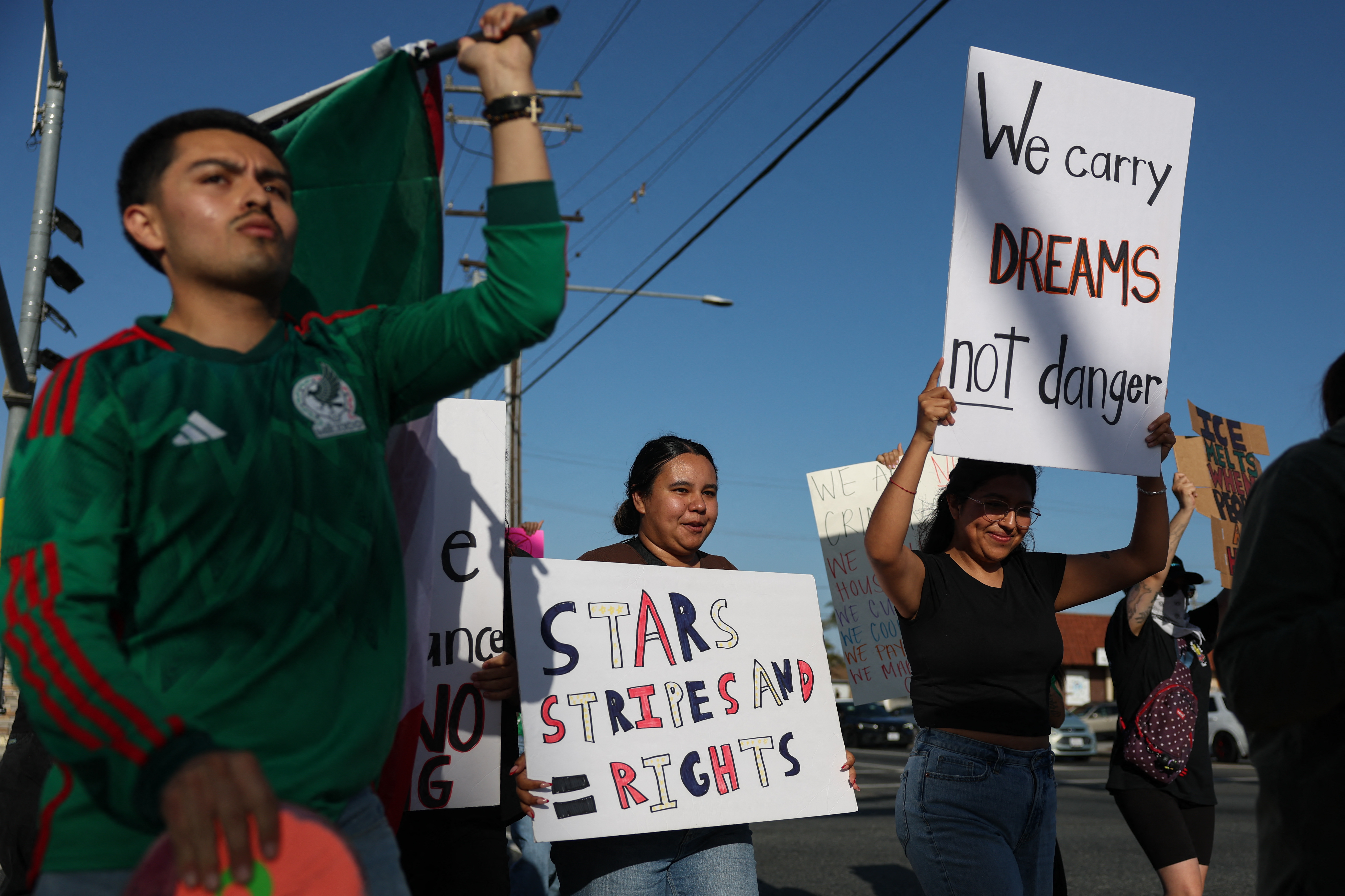 People hold signs as they peacefully protest following social reports of federal immigration operations by Immigration and Customs Enforcement (ICE) in Lawndale, California on June 18, 2025. Calm appeared to be returning to protest-hit Los Angeles on June 17 as the mayor lifted a nighttime curfew, while US President Donald Trump battled to keep control of California troops he deployed to the city. Roughly half of the stores have begun taking down the plywood that had been put up to protect their windows. A fraction of the sprawling US city had been off-limits from 8pm to 6am to most people for a week after instances of looting and vandalism during demonstrations against Trump's immigration raids. (Photo by Patrick T. Fallon / AFP)
