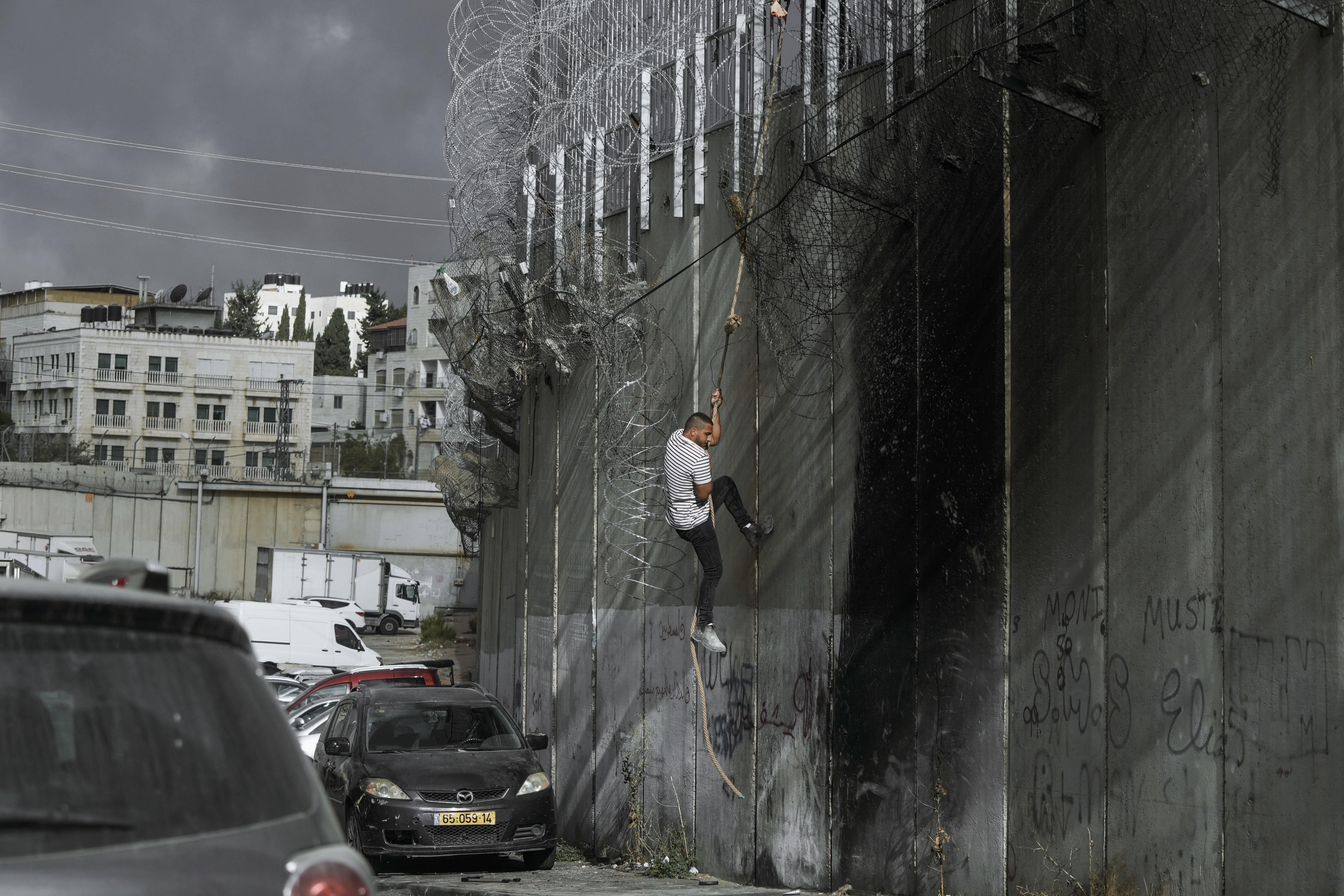 A Palestinian man climbs the separation wall at the town of al-Ram to illegally cross into Jerusalem, Sunday, Sept. 15, 2024. (AP Photo/Mahmoud Illean)