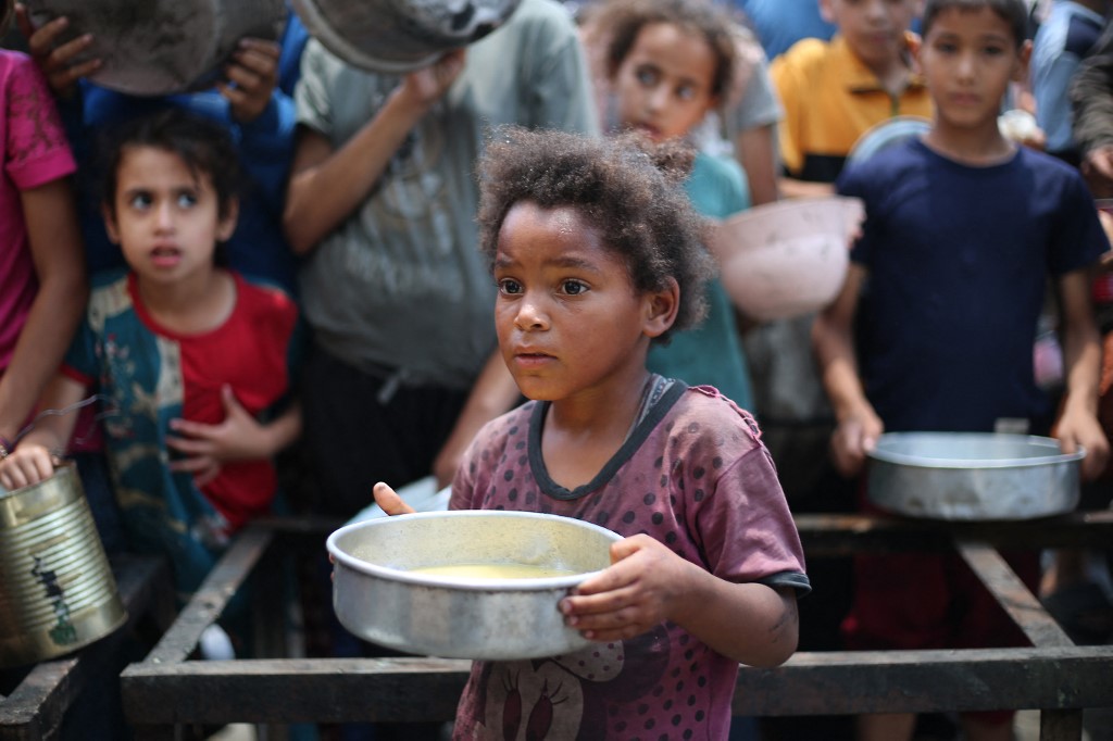 Palestinian children line up to receive a hot meal at a food distribution point.