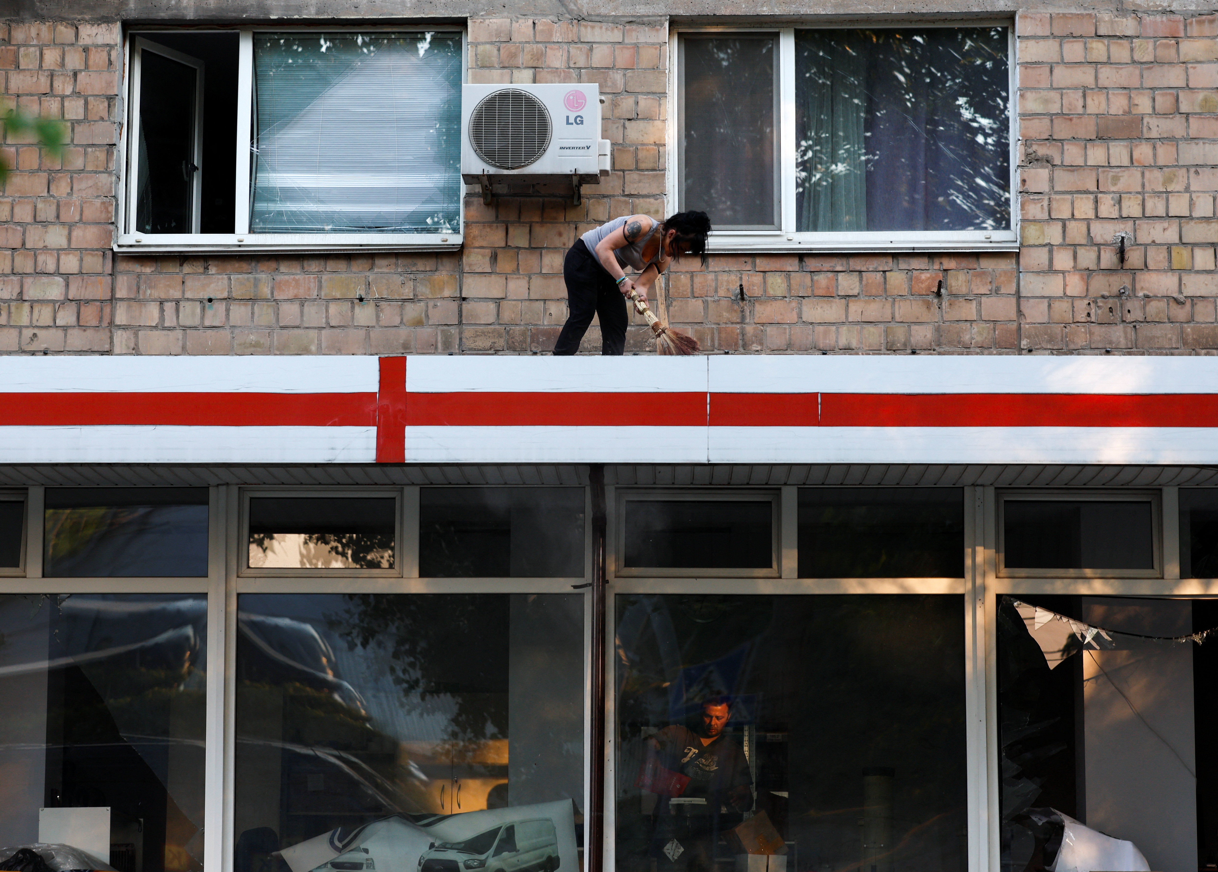 A woman sweeps the veranda of a building, damaged during Russian drone and missile attacks.