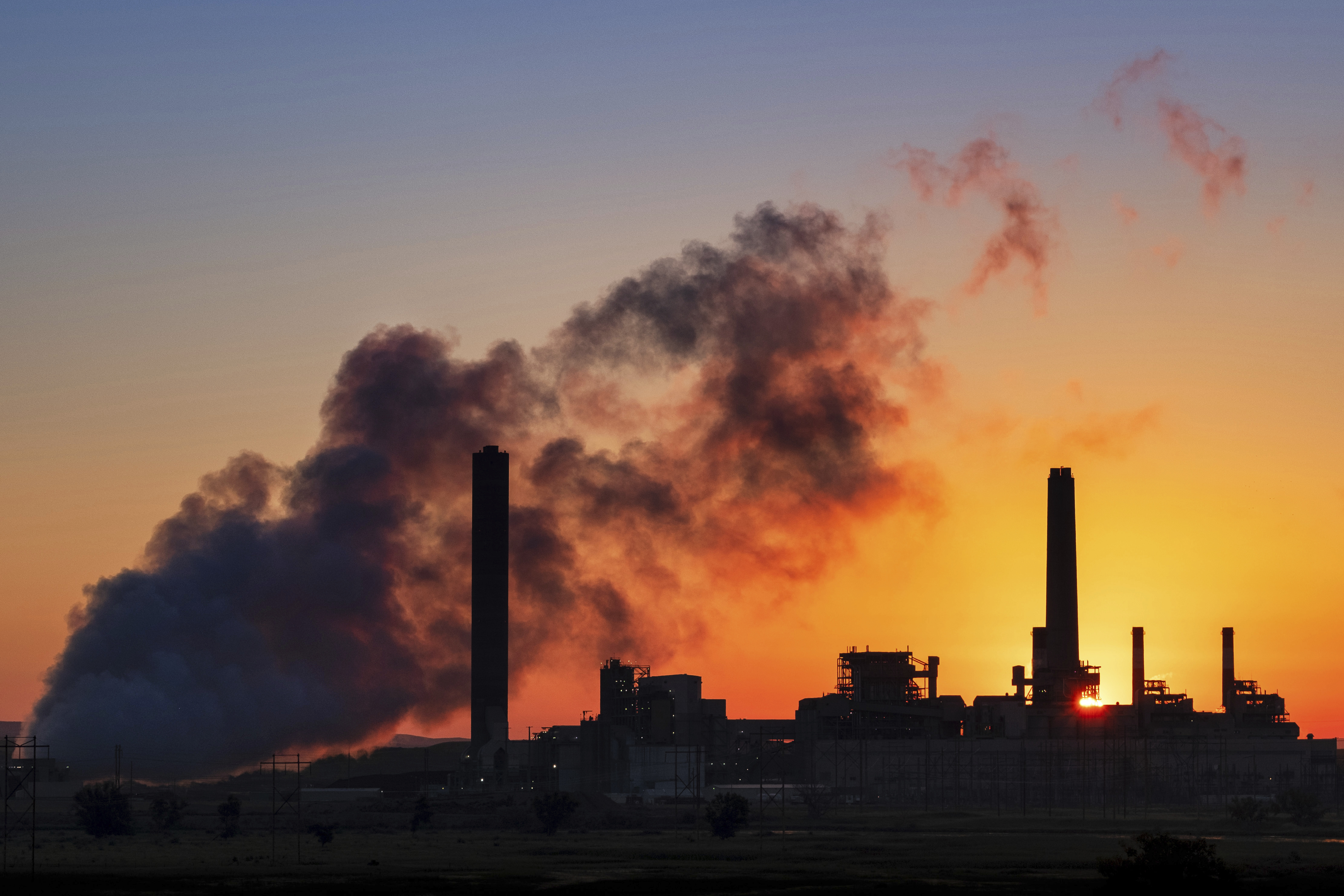 The silhouette of a coal-powered energy plant in Glenrock, Wyoming, with billowing smoke against a fiery sunrise.