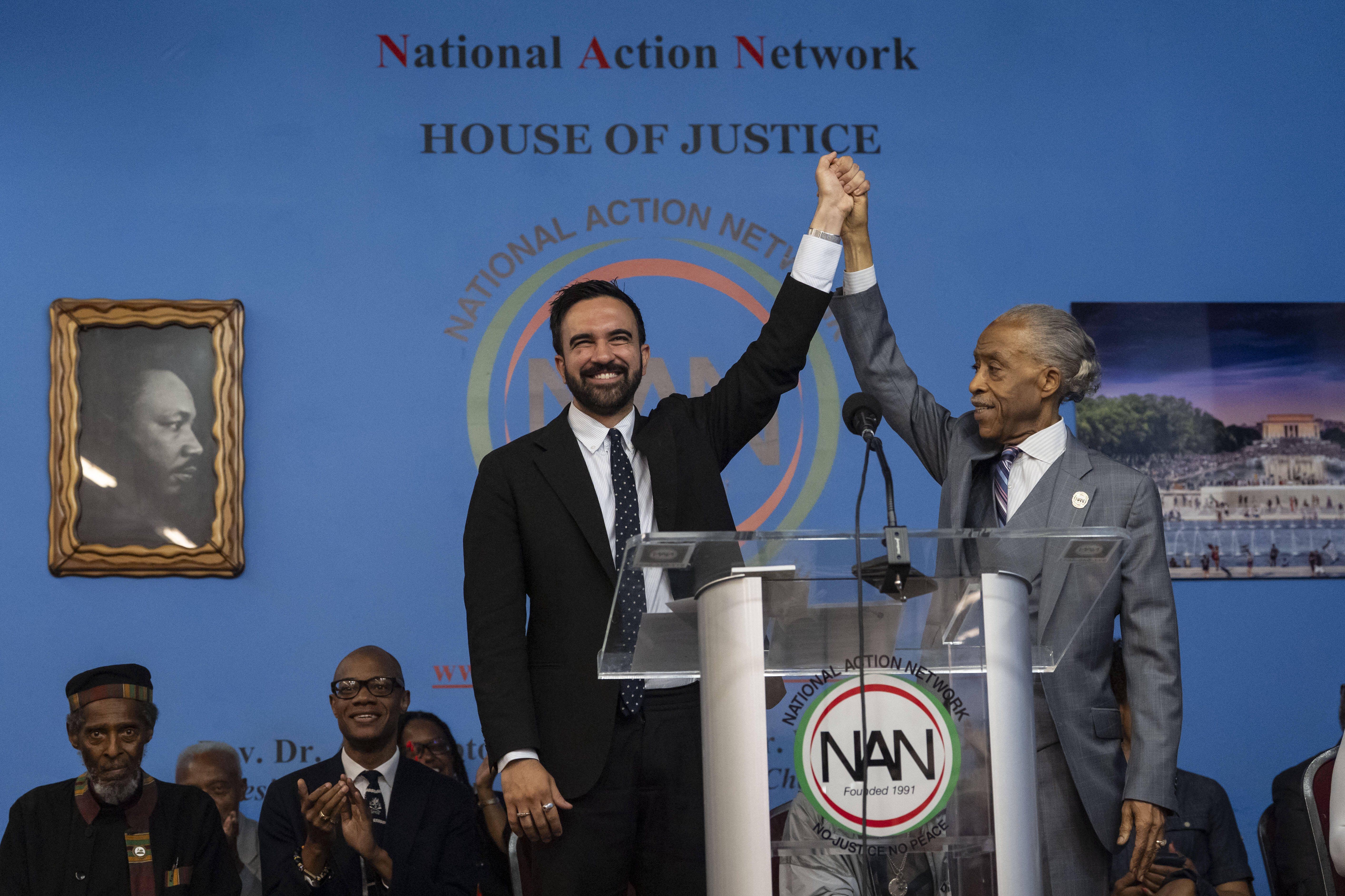 Al Sharpton raises the hand of Zohran Mamdani behind a podium for the National Action Network.