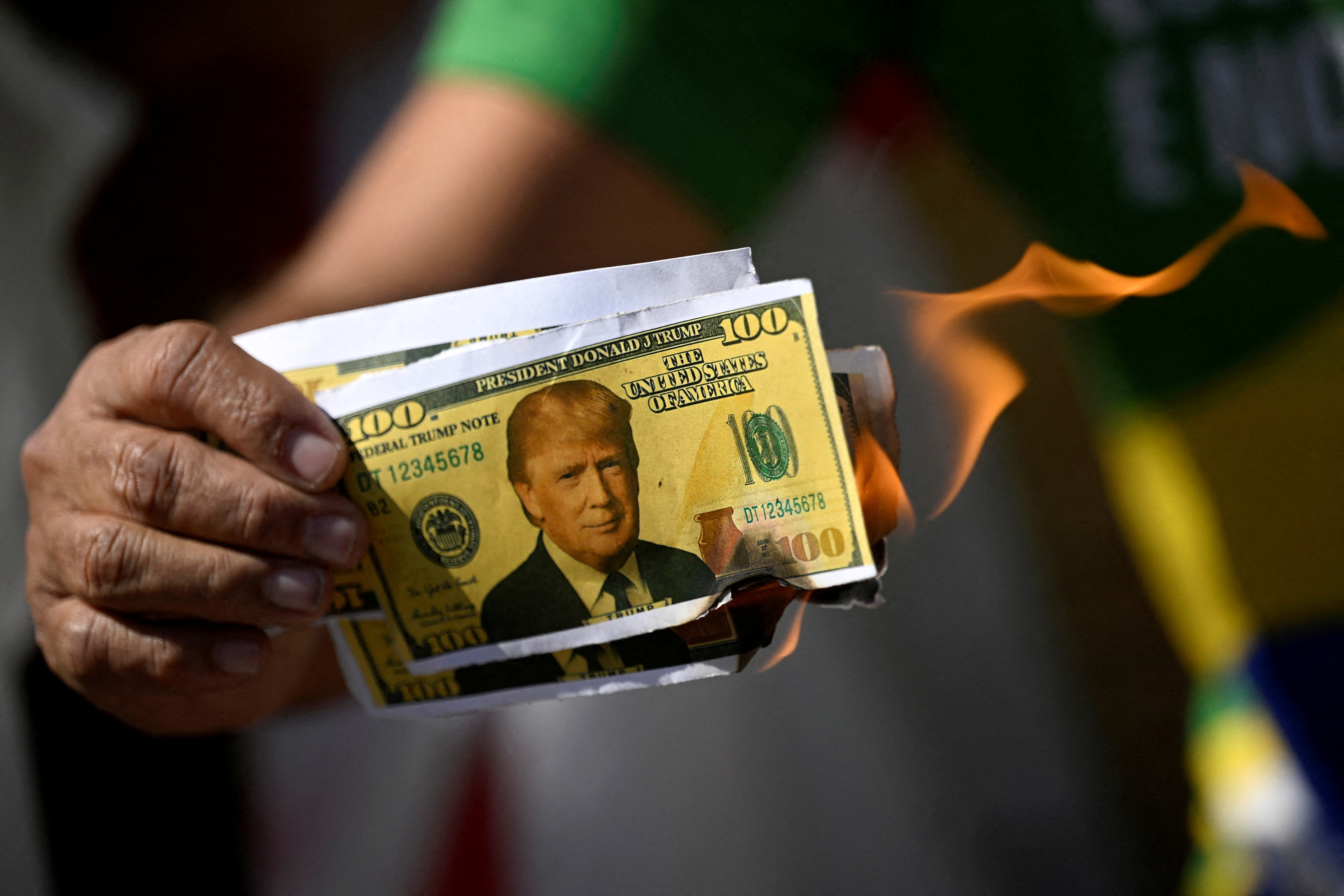 A person holds up fake Trump currency as it burns.