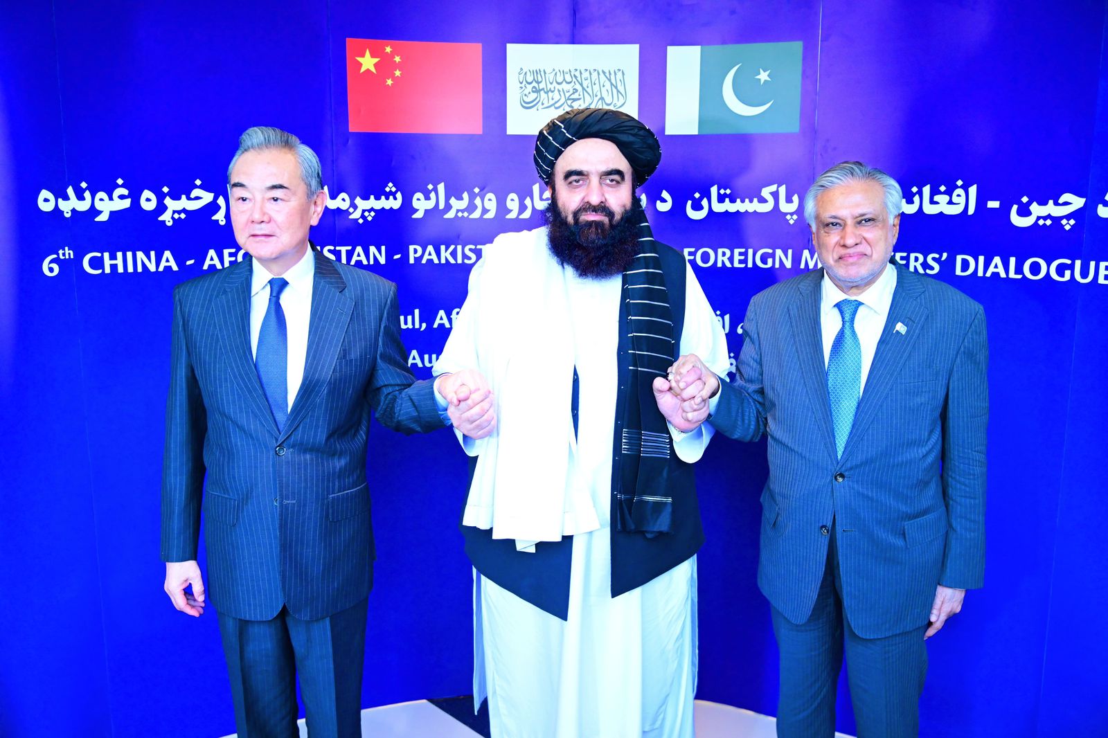 Wang Yi, Amir Khan Muttaqi and Ishaq Dar hold hands and pose for a photo.