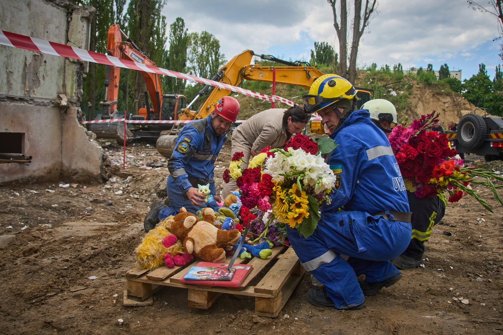 people wearing emergency uniforms lay flowers and teddy bears next to a destroyed building