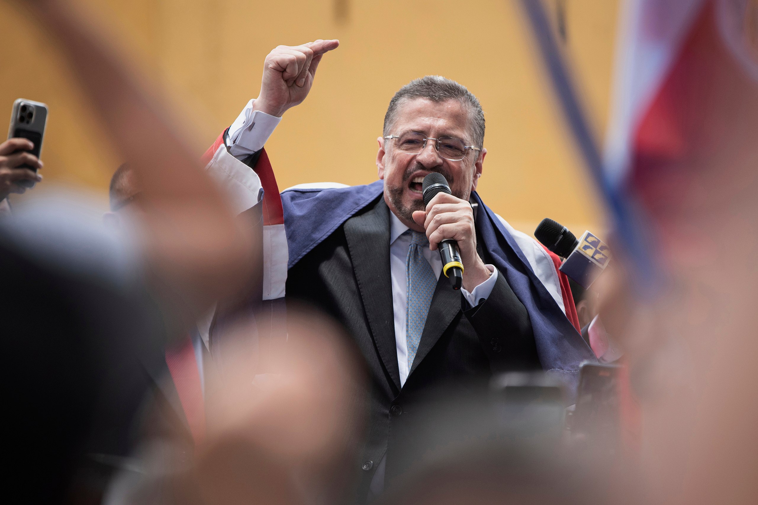 Rodrigo Chaves Robles lifts a finger into the air as he speaks into a microphone to his supporters.