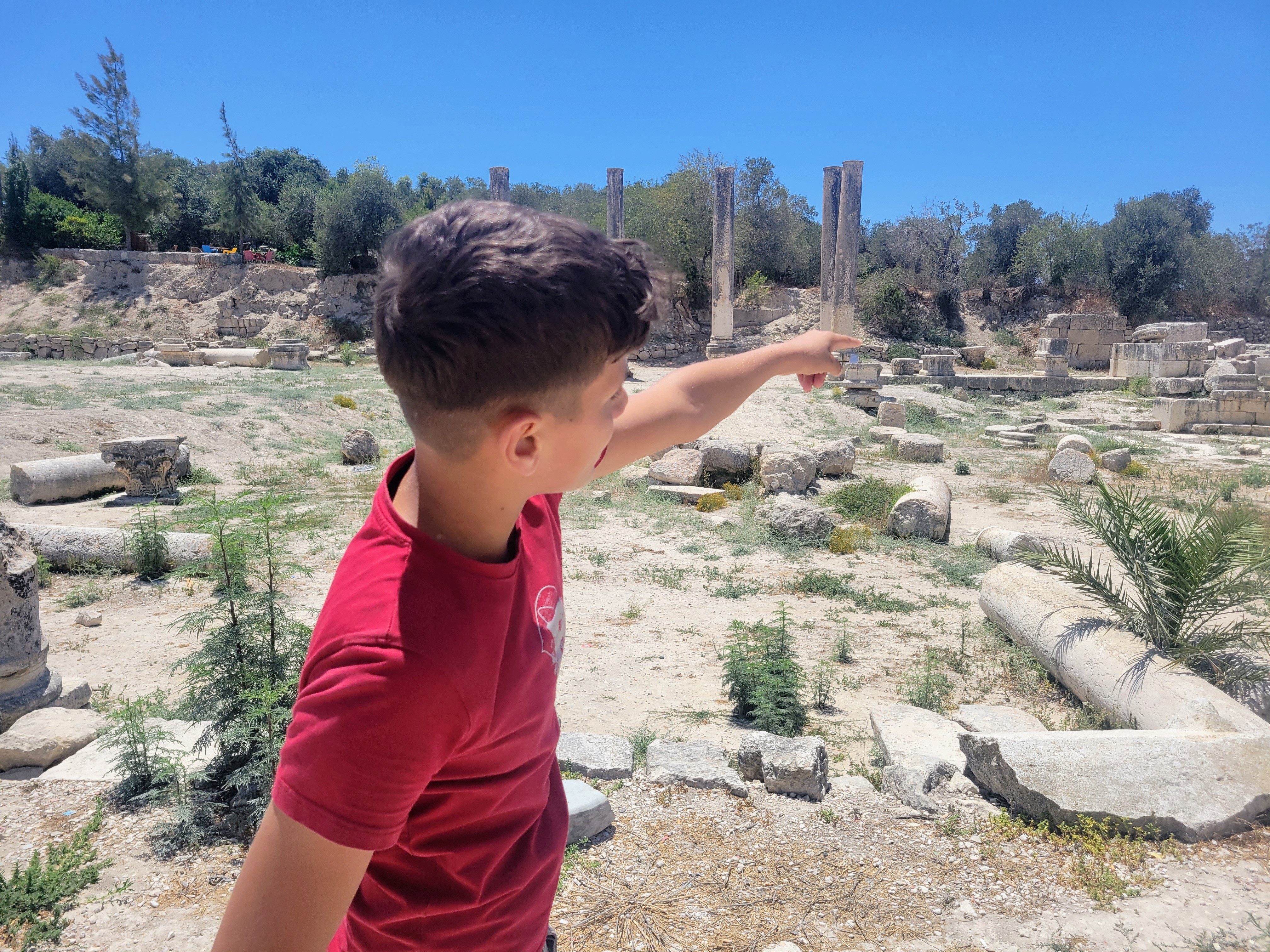 A little boy in a red t-shirt points at a corner of the Sebastia ruins where he likes to play