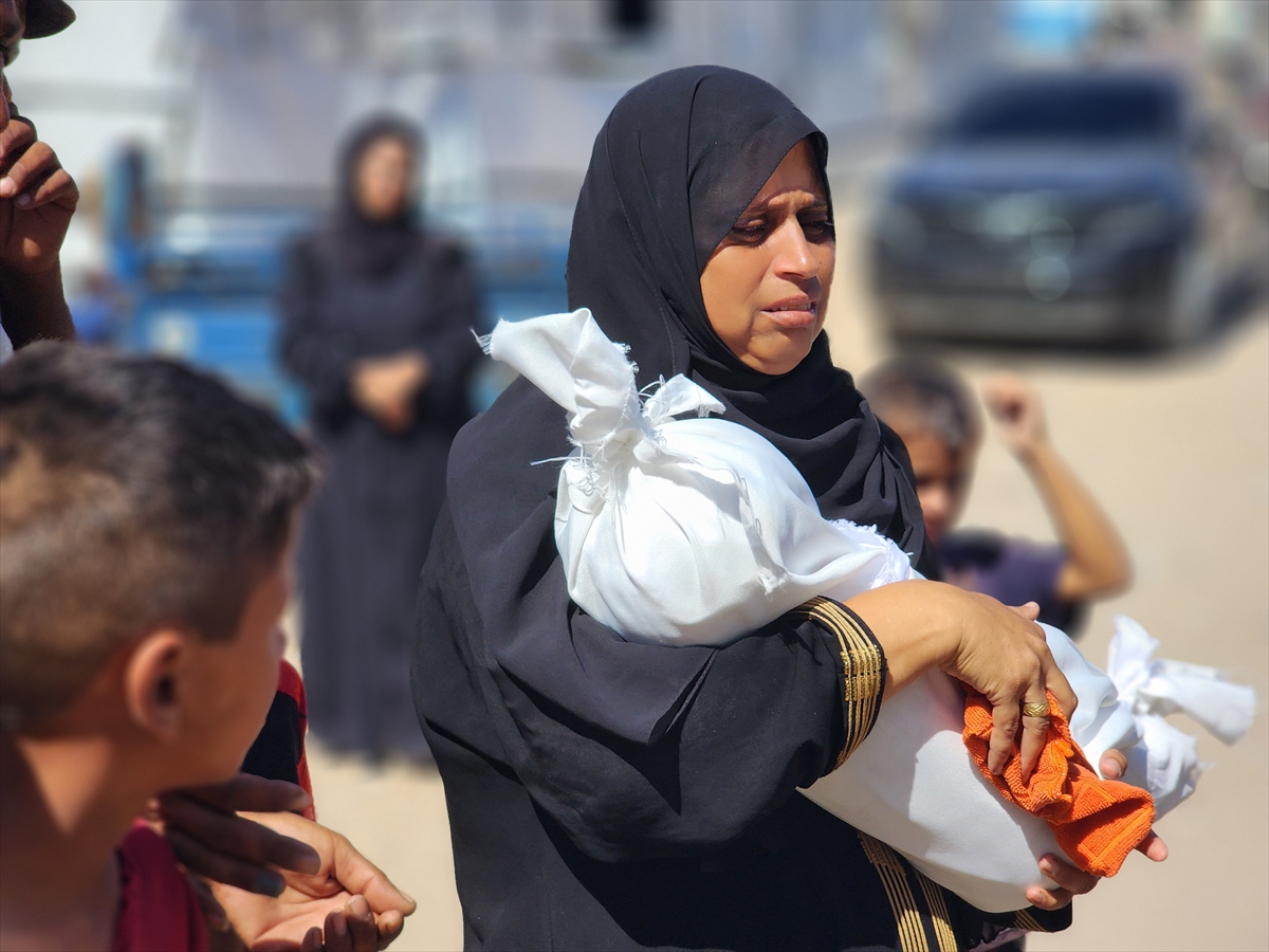 a woman holds the body of a small child wrapped in white cloth