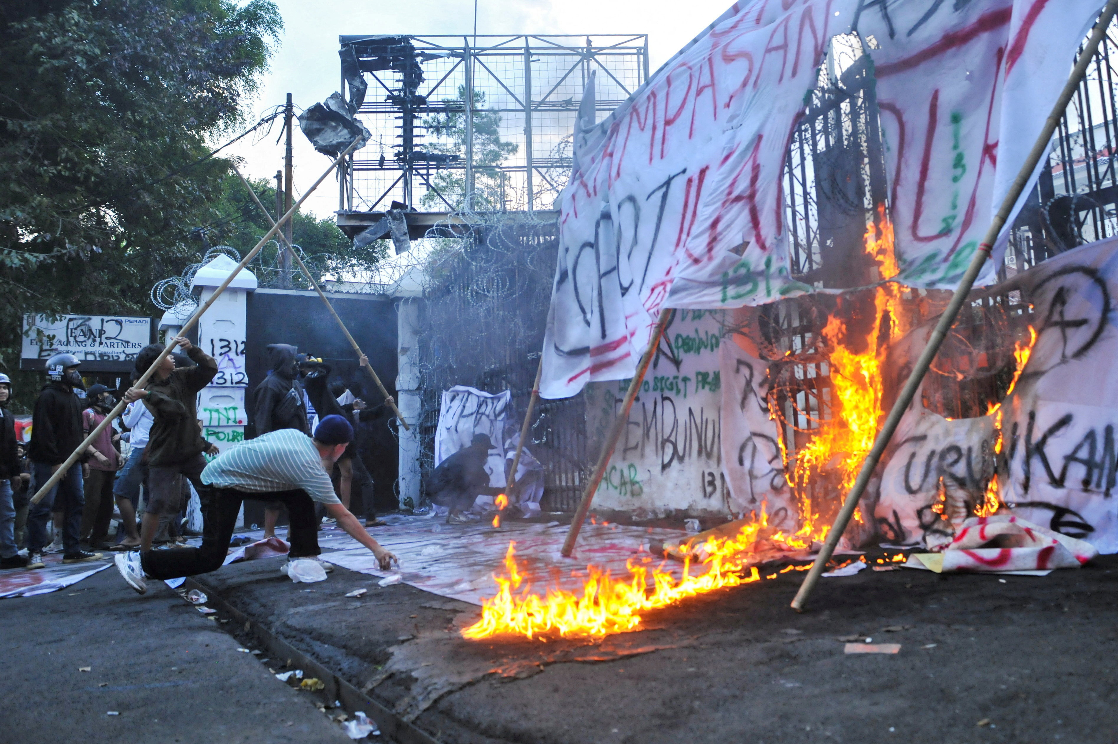 Protesters throw bamboo sticks while setting banners on fire at the gate of the regional parliament building in Bandung, West Java province, Indonesia