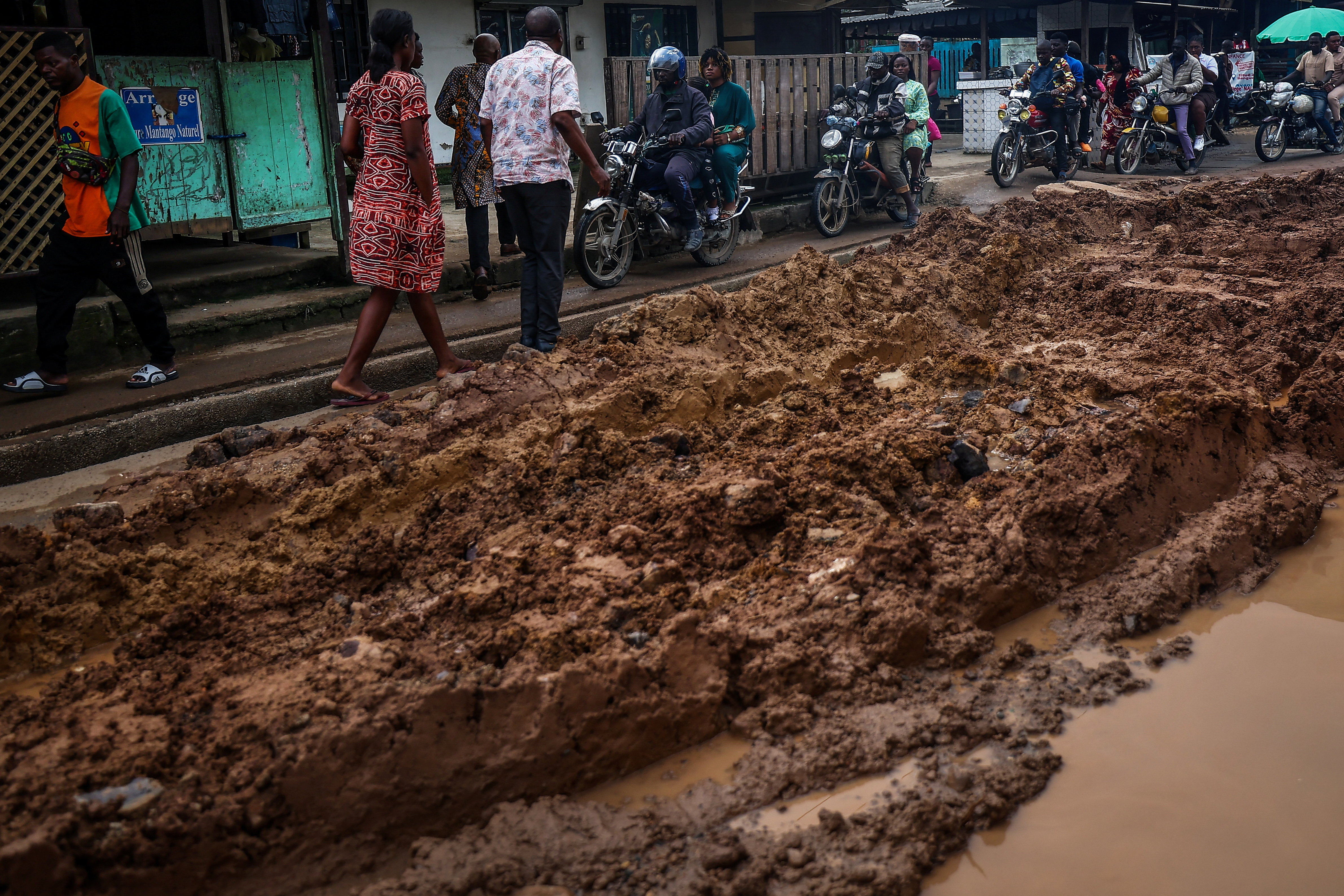 People walk past motorcycle taxi riders along a muddy road in Douala, Cameroon, on October 4, 2025 [Reuters]