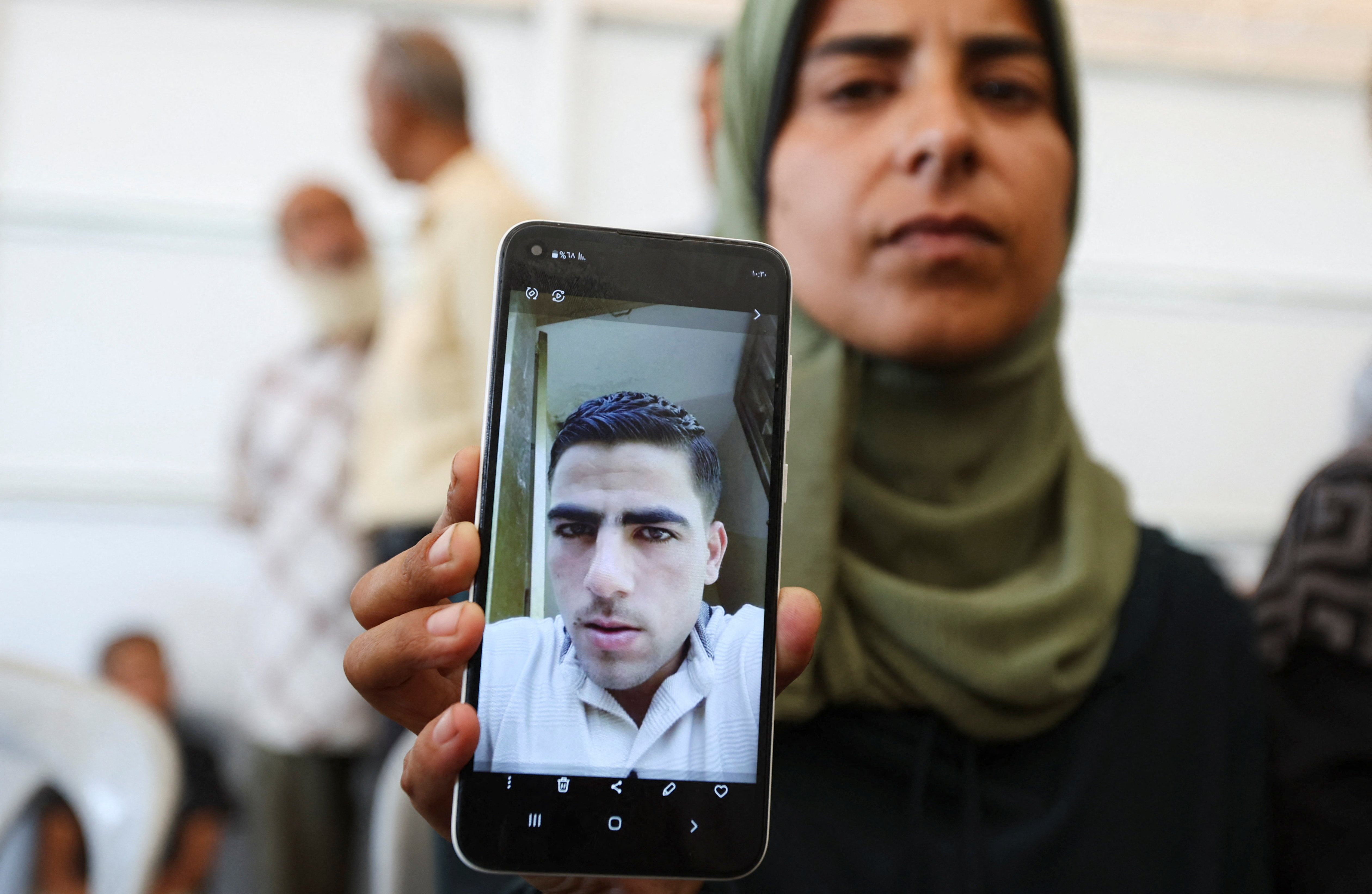 A Palestinian woman holds up a photo of her husband on her cell phone, in Gaza