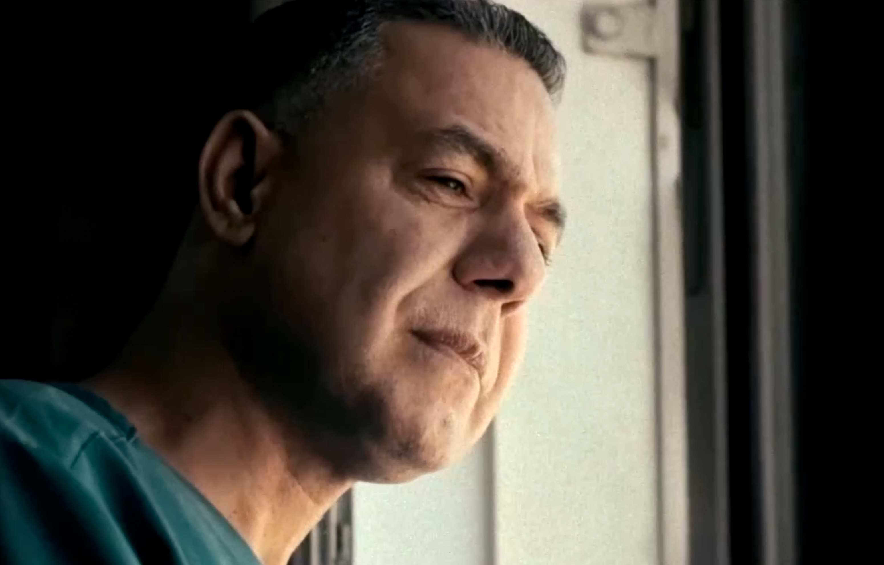 Dr hossam Abu Safia wearing green scrubs, looking out of a window in the hospital, his face partially lit