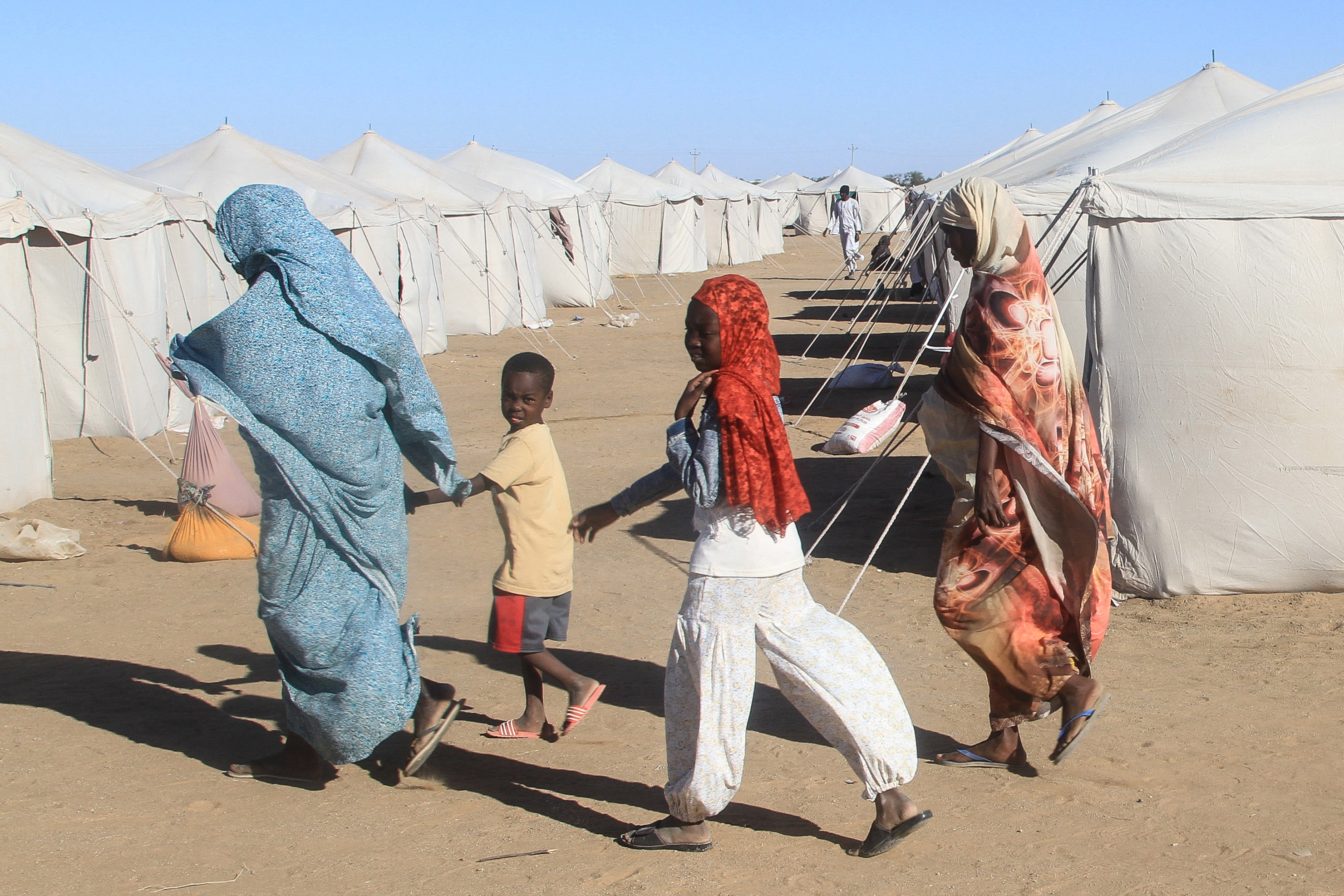 Sudanese who fled El-Fasher walk past tents at a camp for displaced people.