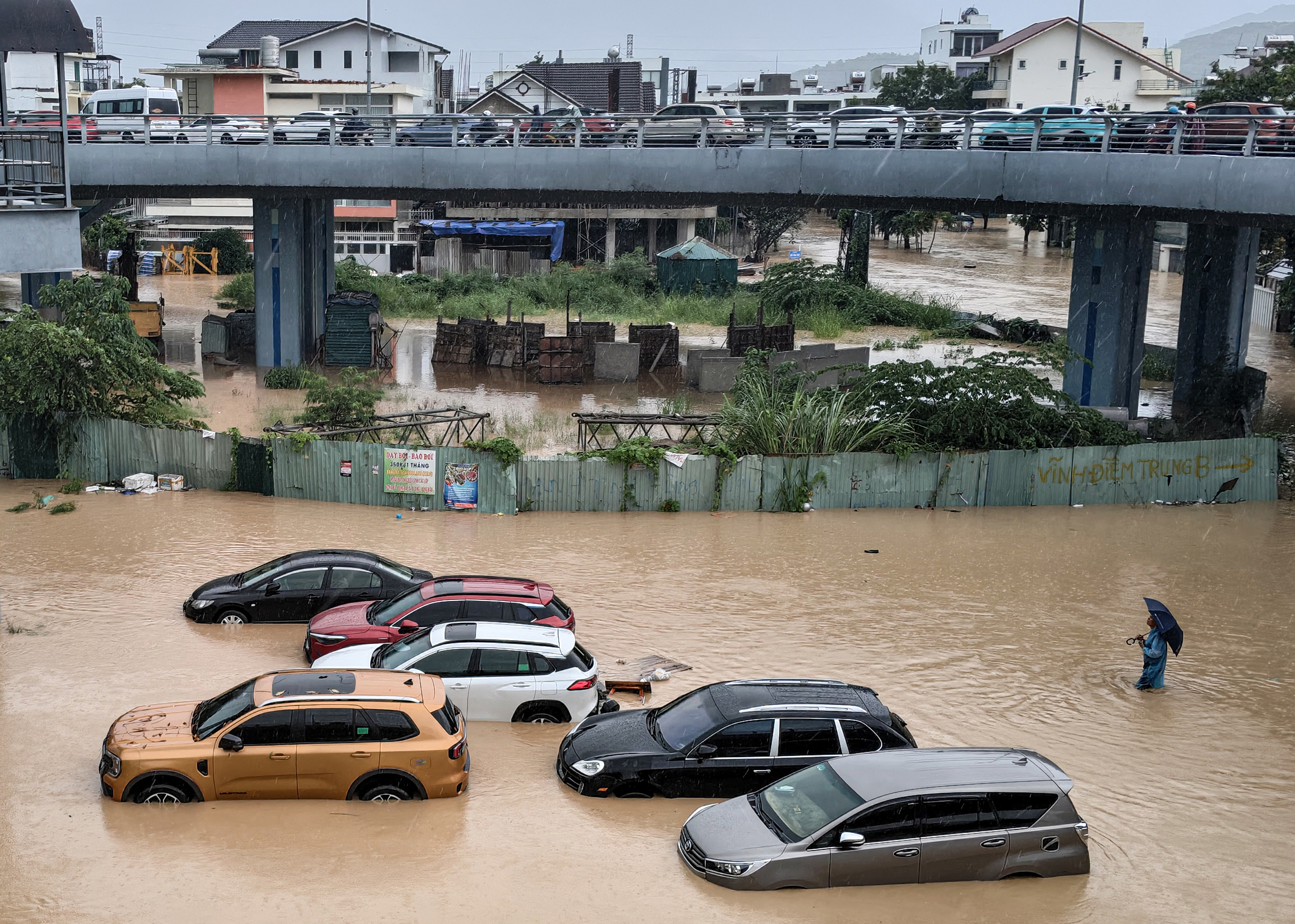 TOPSHOT - A man (R) wades through floodwaters near inundated vehicles in Nha Trang, Vietnam's coastal province of Khanh Hoa on November 20, 2025.