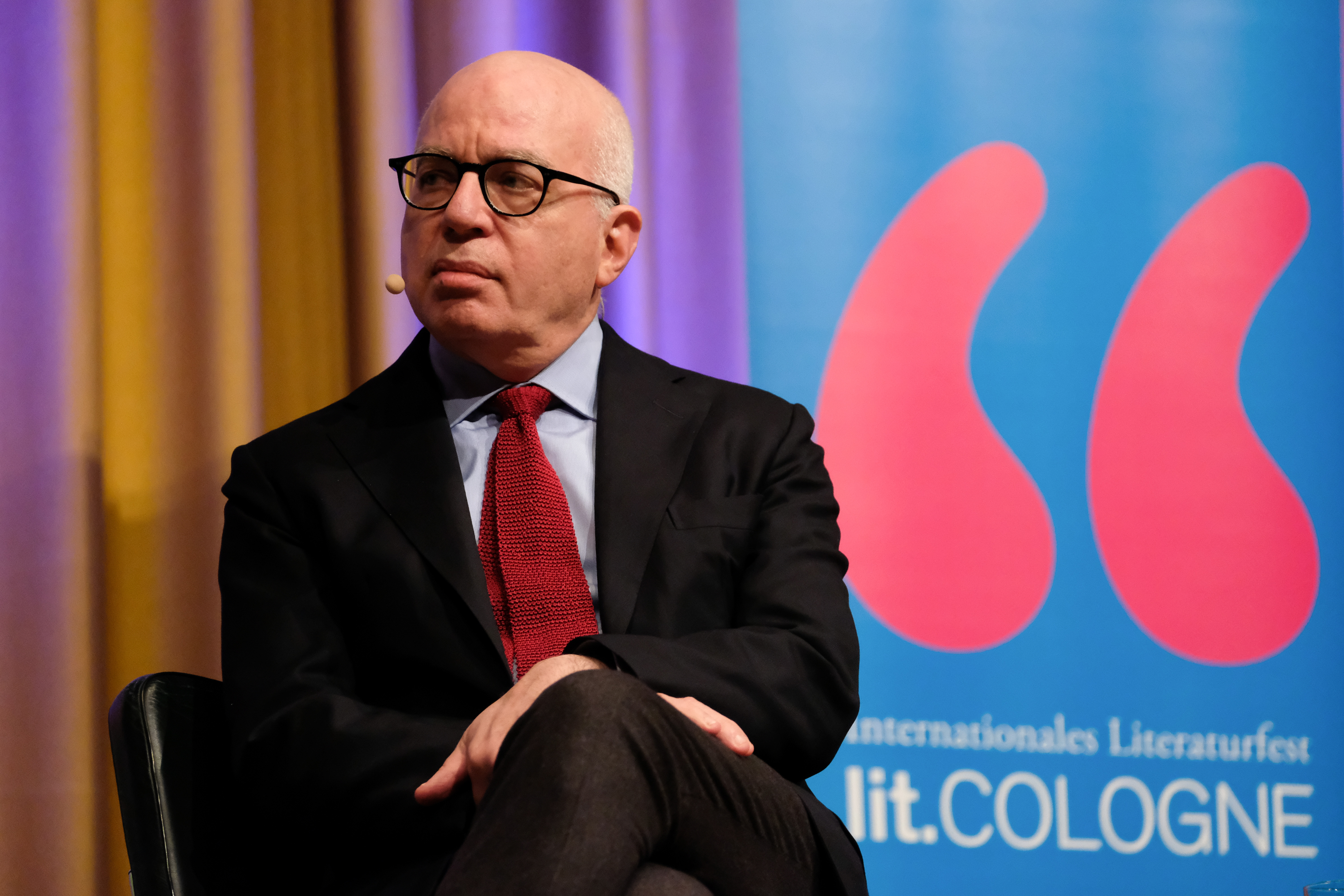 Michael Wolff during a book reading with the logo of Cologne, Germany on a poster behind him.