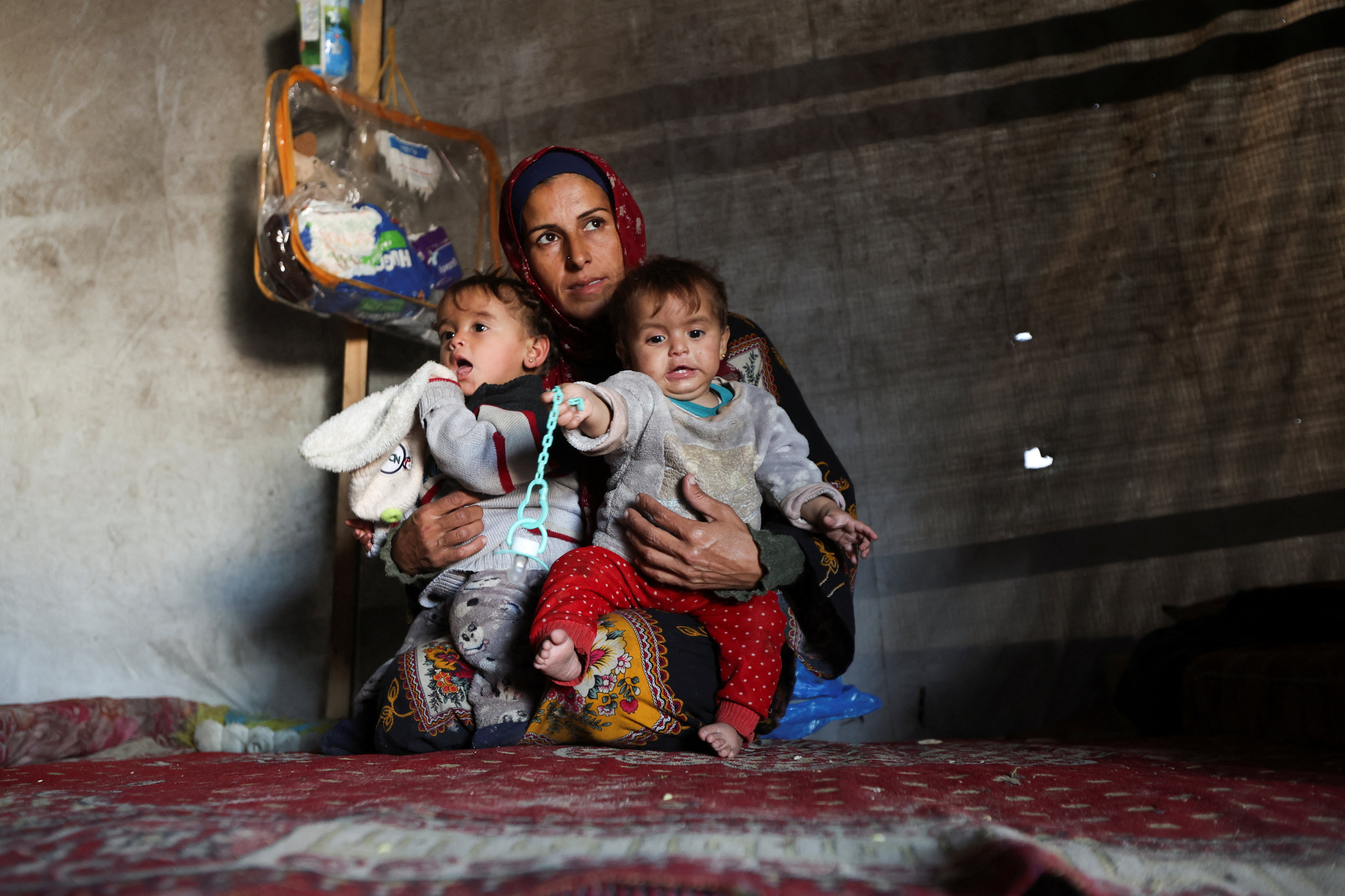 Displaced Palestinian woman Hanan Abu Taibah holds her children inside a tent as families struggle to stay warm during winter, in Khan Younis, southern Gaza Strip, December 18, 2025. [Ramadan Abed/Reuters]