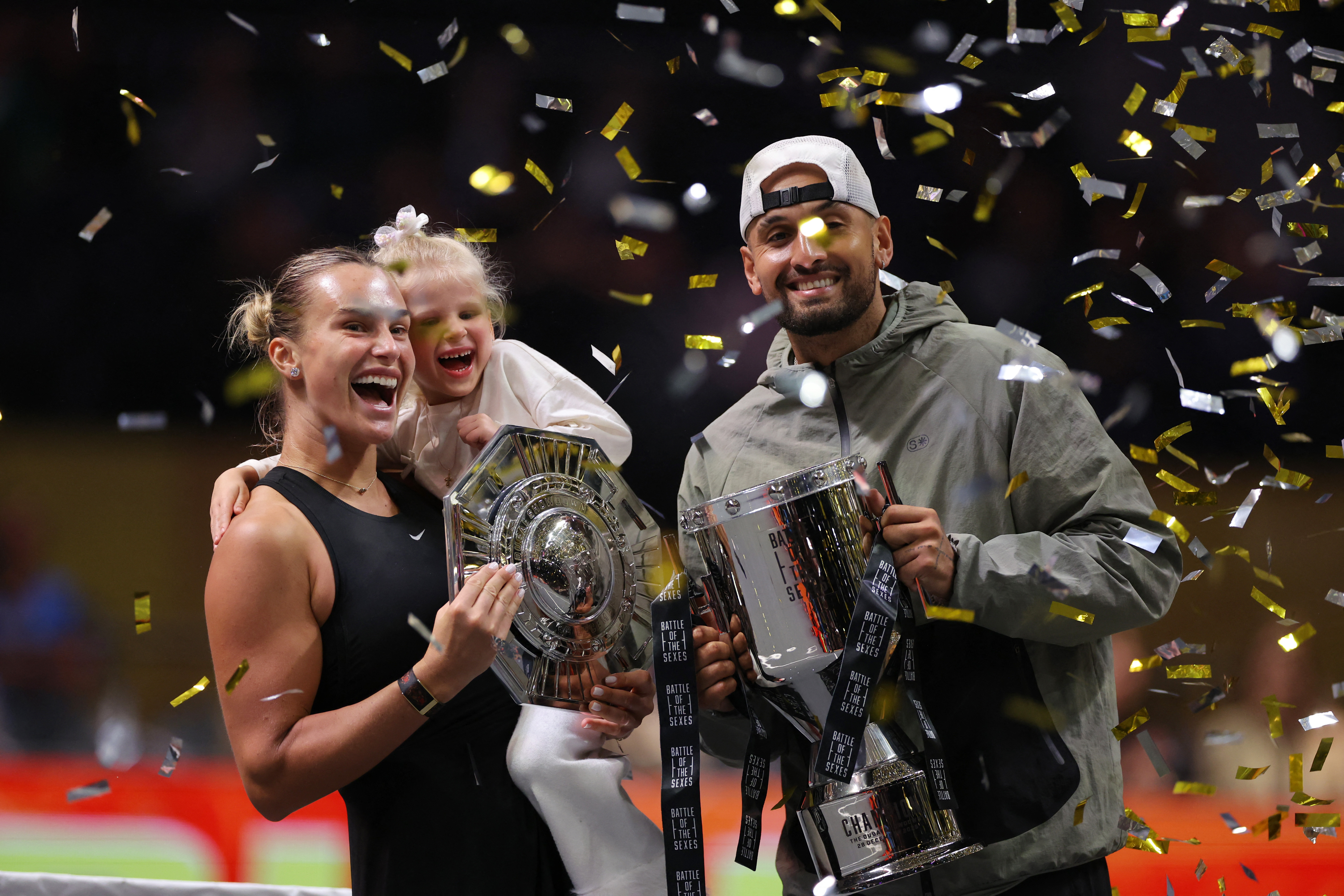 Tennis - 'Battle of the Sexes' - Nick Kyrgios v Aryna Sabalenka - Coca-Cola Arena, Dubai, United Arab Emirates - December 28, 2025 Belarus' Aryna Sabalenka, her goddaughter Nicole, and Australia's Nick Kyrgios celebrate with trophies after the match REUTERS/Amr Alfiky/Pool