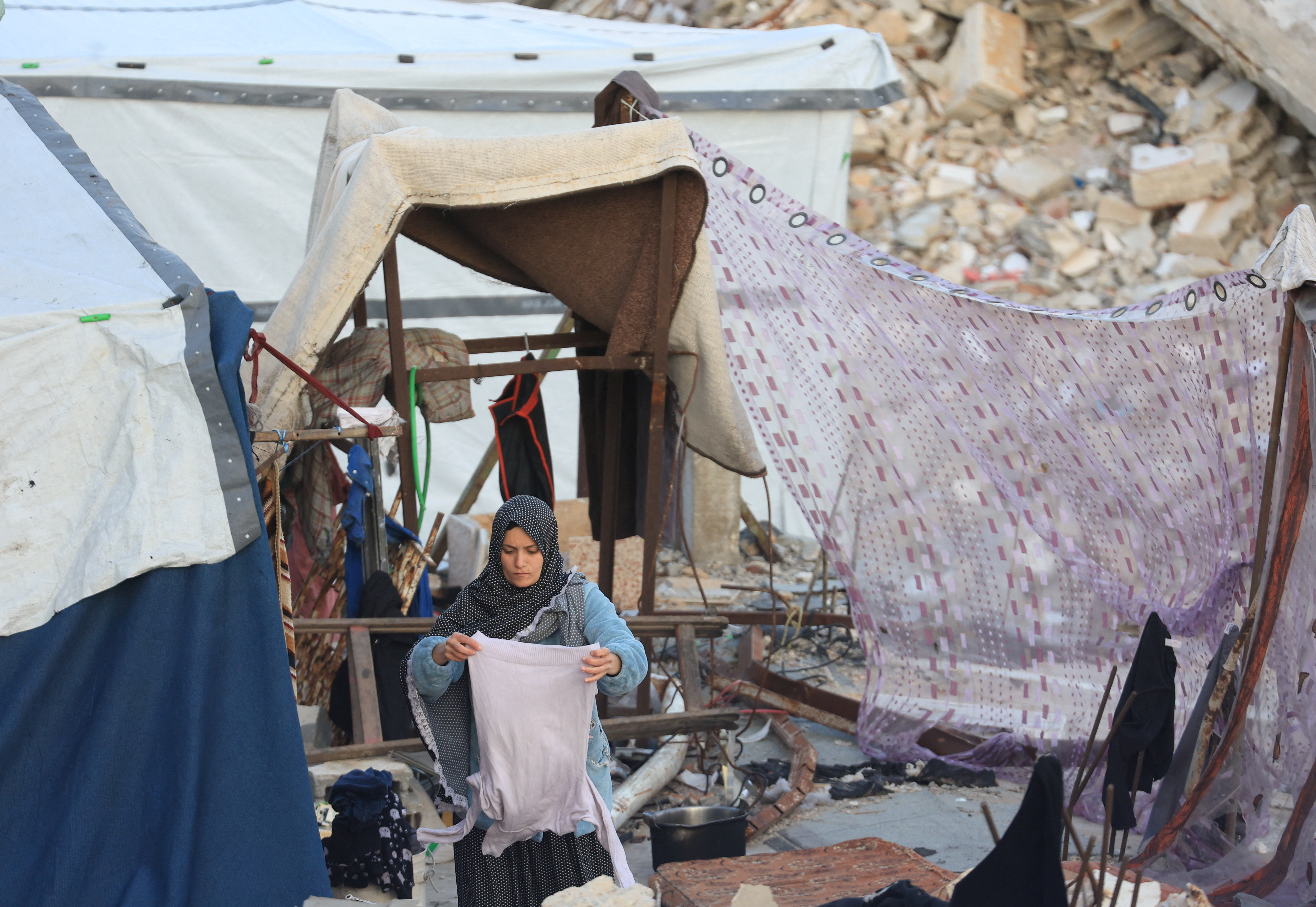 A Palestinian woman holds a shirt outside a tent, near the rubble of residential buildings destroyed during the war