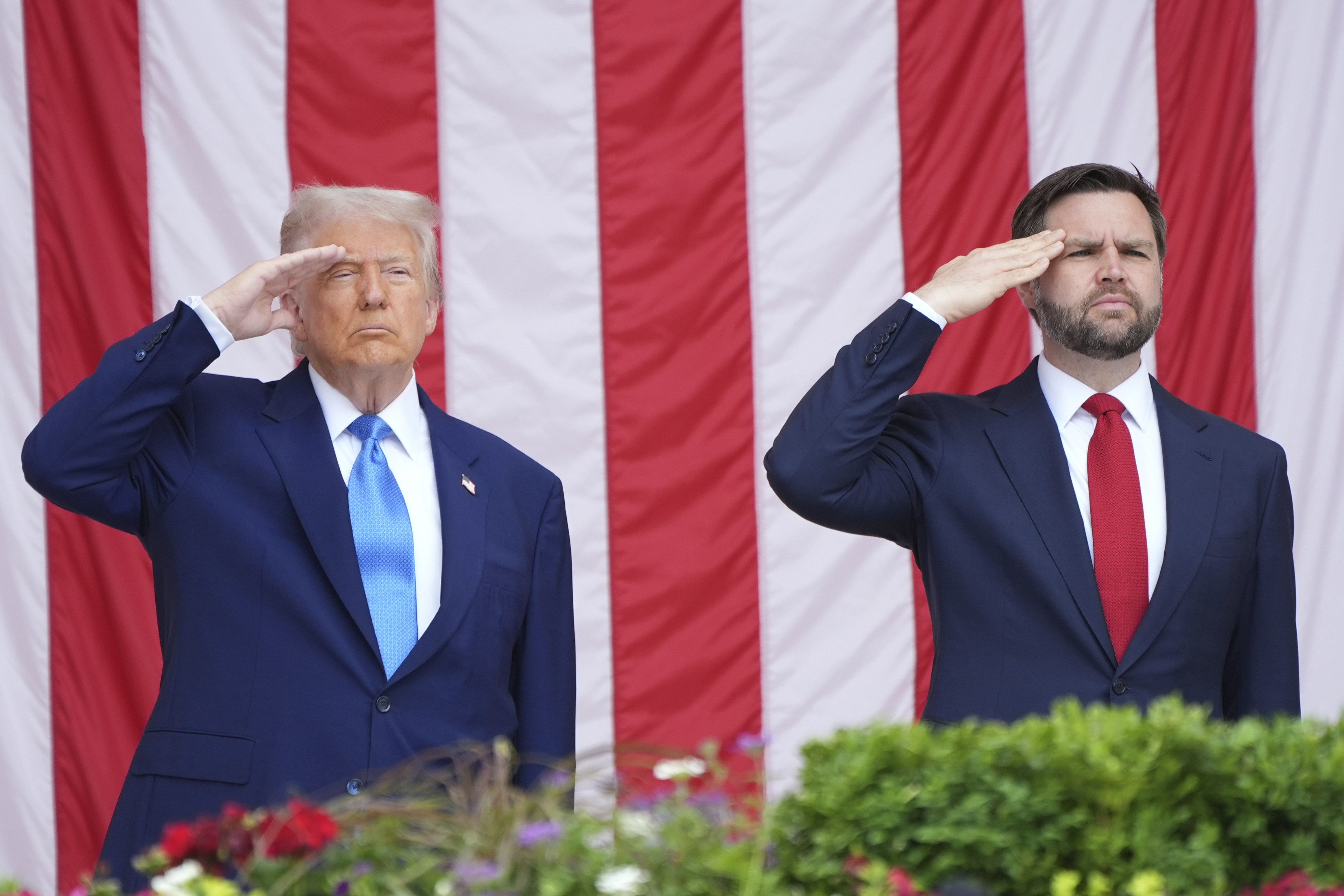 Trump and JD Vance salute in front of a US flag