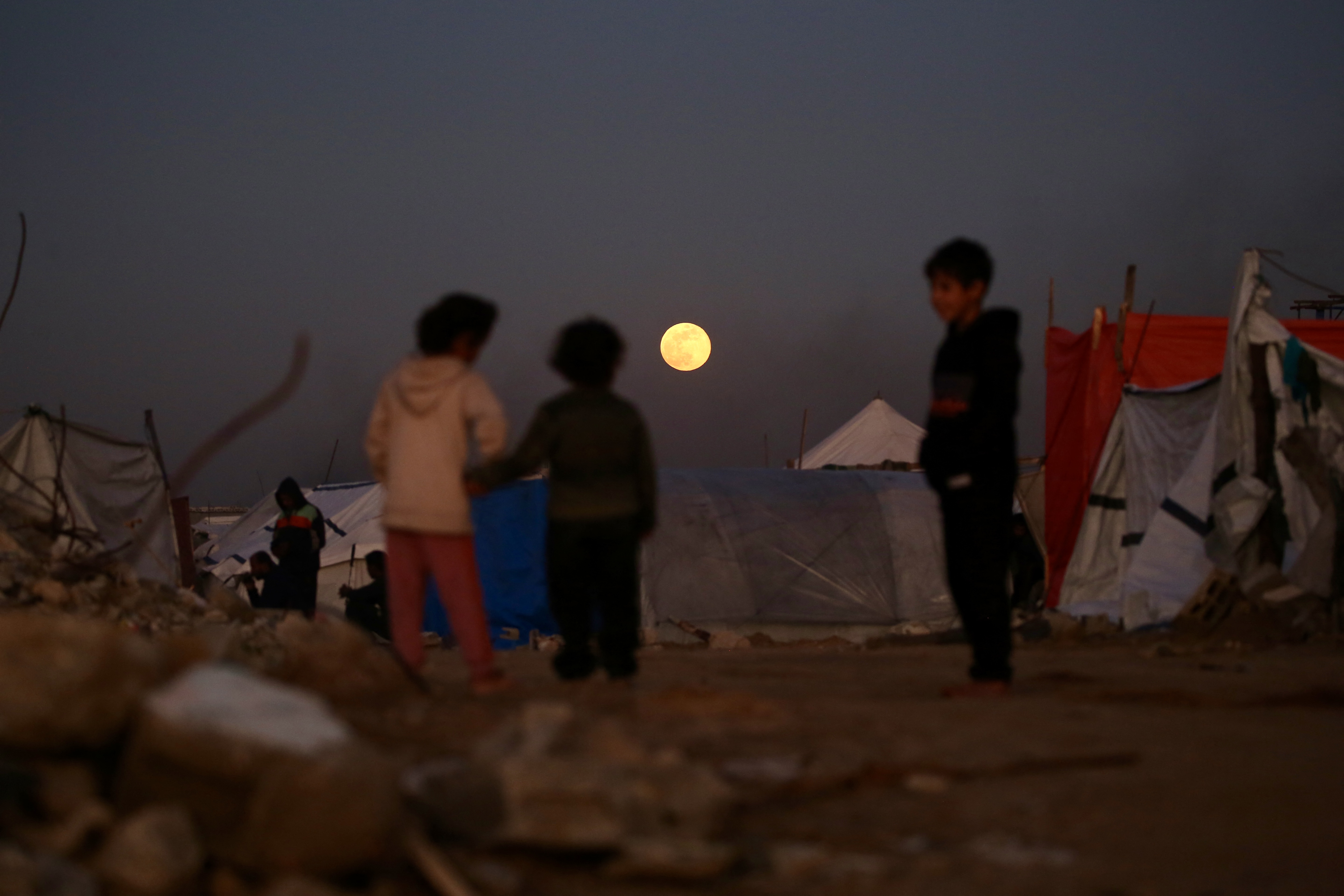Displaced Palestinian children interact as the first supermoon of the year, the ‘Wolf Moon,’ rises over Bureij refugee camp, in the central Gaza Strip on January 3, 2026. (Photo by Eyad Baba / AFP)