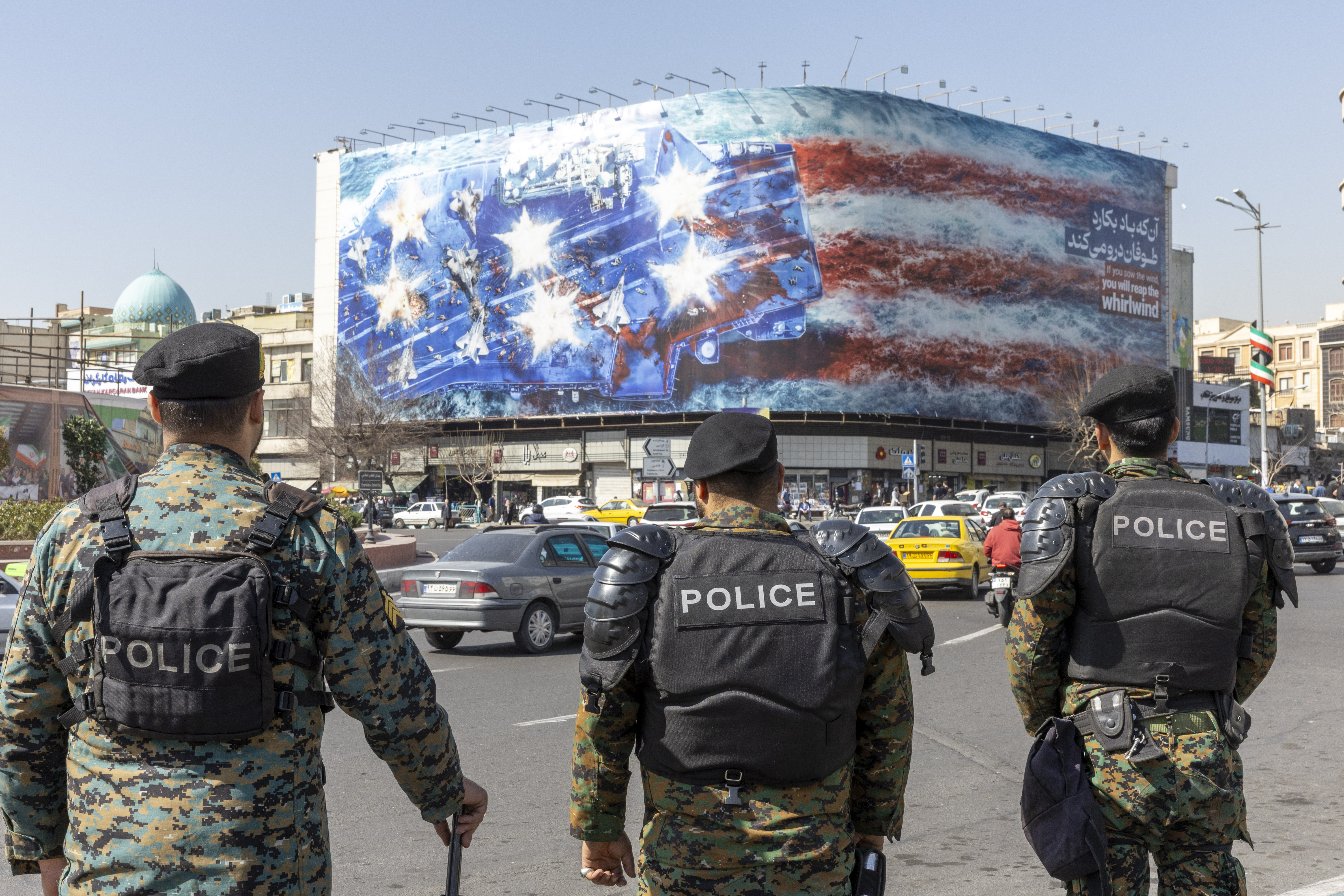 TEHRAN, IRAN - FEBRUARY 21: Anti riot police stand in front of state building that is covered with a giant anti-U.S. billboard depicting the destruction of a US aircraft carrier in downtown Tehran on a main street in Tehran on February 21, 2026 in Tehran, Iran. In recent weeks, the United States has moved vast numbers of military vessels and aircraft to Europe and the Middle East, heightening speculation that it intended to strike Iran. (Photo by Majid Saeedi/Getty Images)