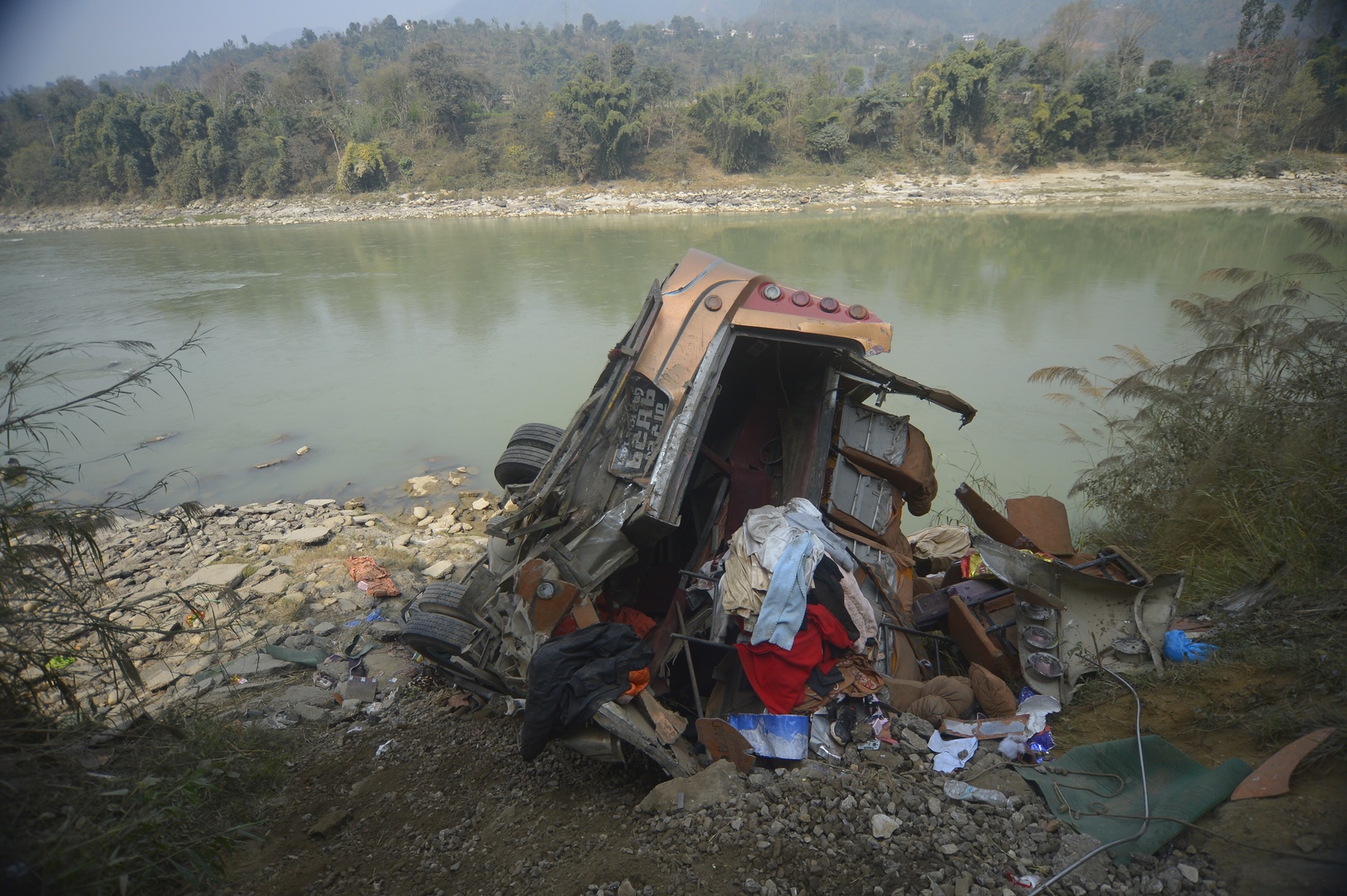 The wreckage of a bus is seen on the bank of the Trishuli River after it drove off a mountain highway near Benighat, west of the capital, Kathmandu, Nepal on Feb. 23, 2026. [Bijay Rai/AP]