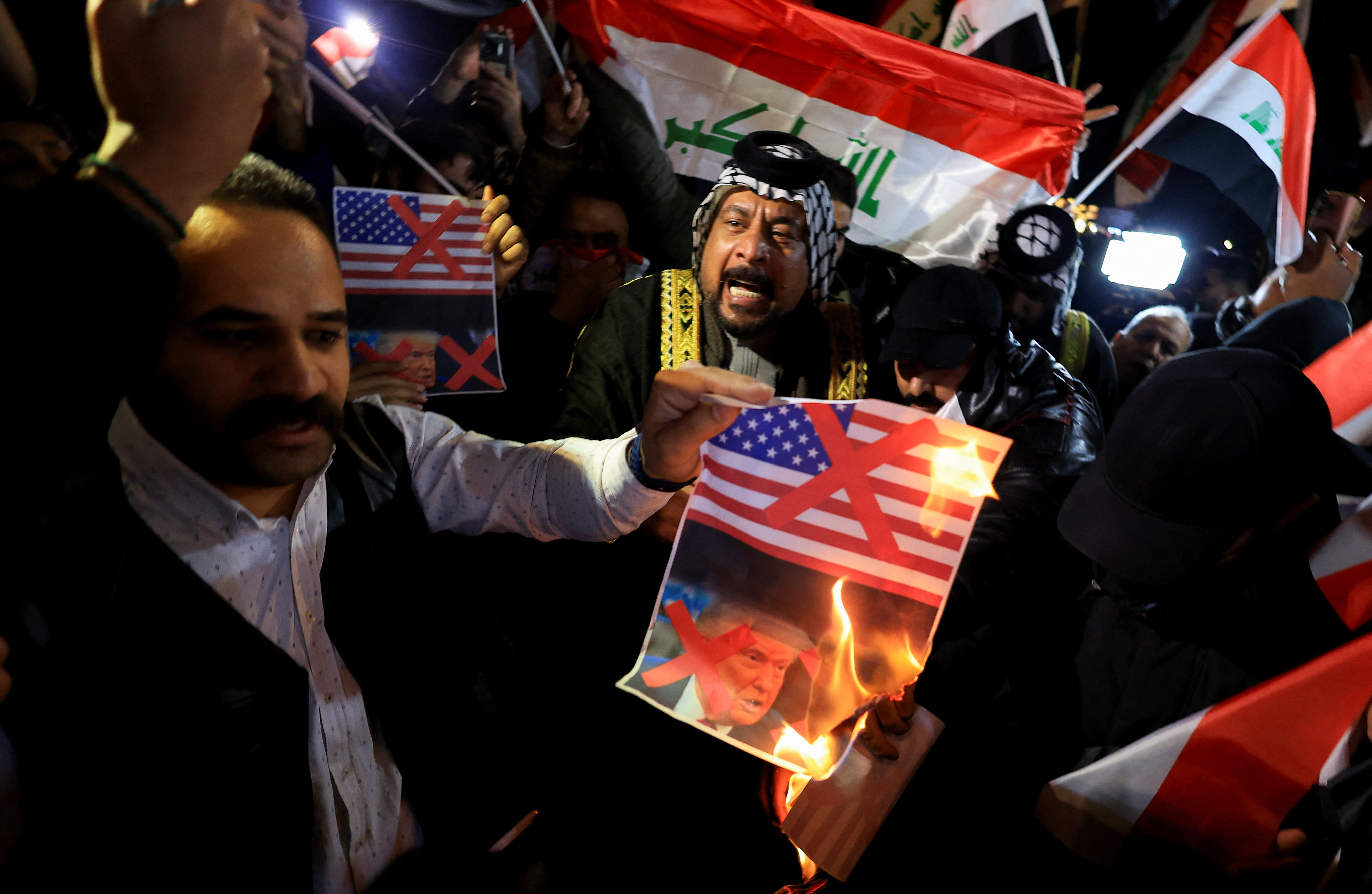 A supporter of Iraqi Shi'ite armed groups burns a poster with red X marks on the images of a U.S. flag and U.S. President Donald Trump during a protest against what they say is U.S. interference in Iraq’s sovereignty near the entrance of the Green Zone, home to the U.S. embassy and other missions, in Baghdad,Iraq, January 28, 2026. REUTERS/Thaier Al-Sudani