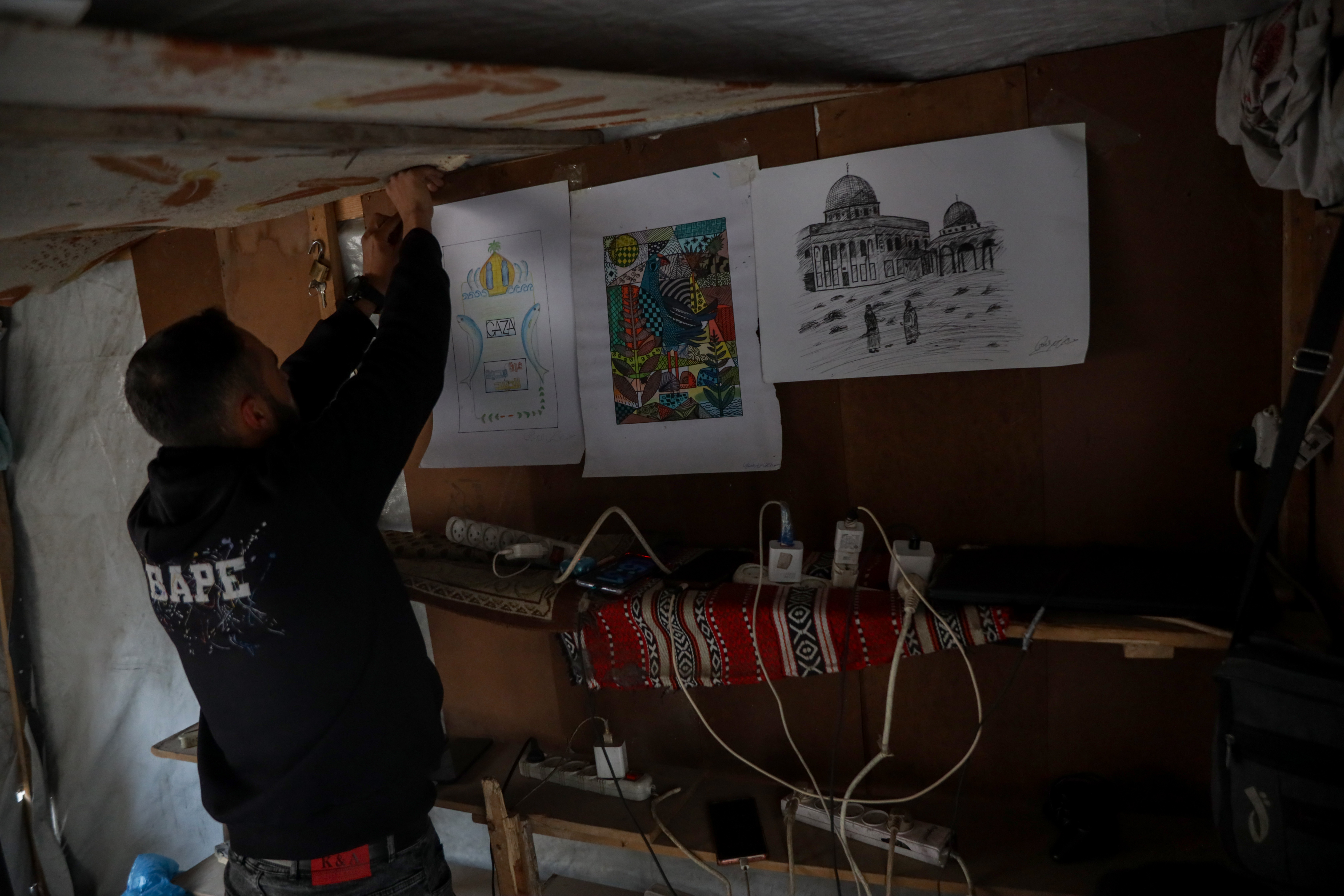Abdulrahman hangs what remains of his artwork inside the charging point, which now serves as his source of income [Abdelhakim Abu Riash/ Al Jazeera]