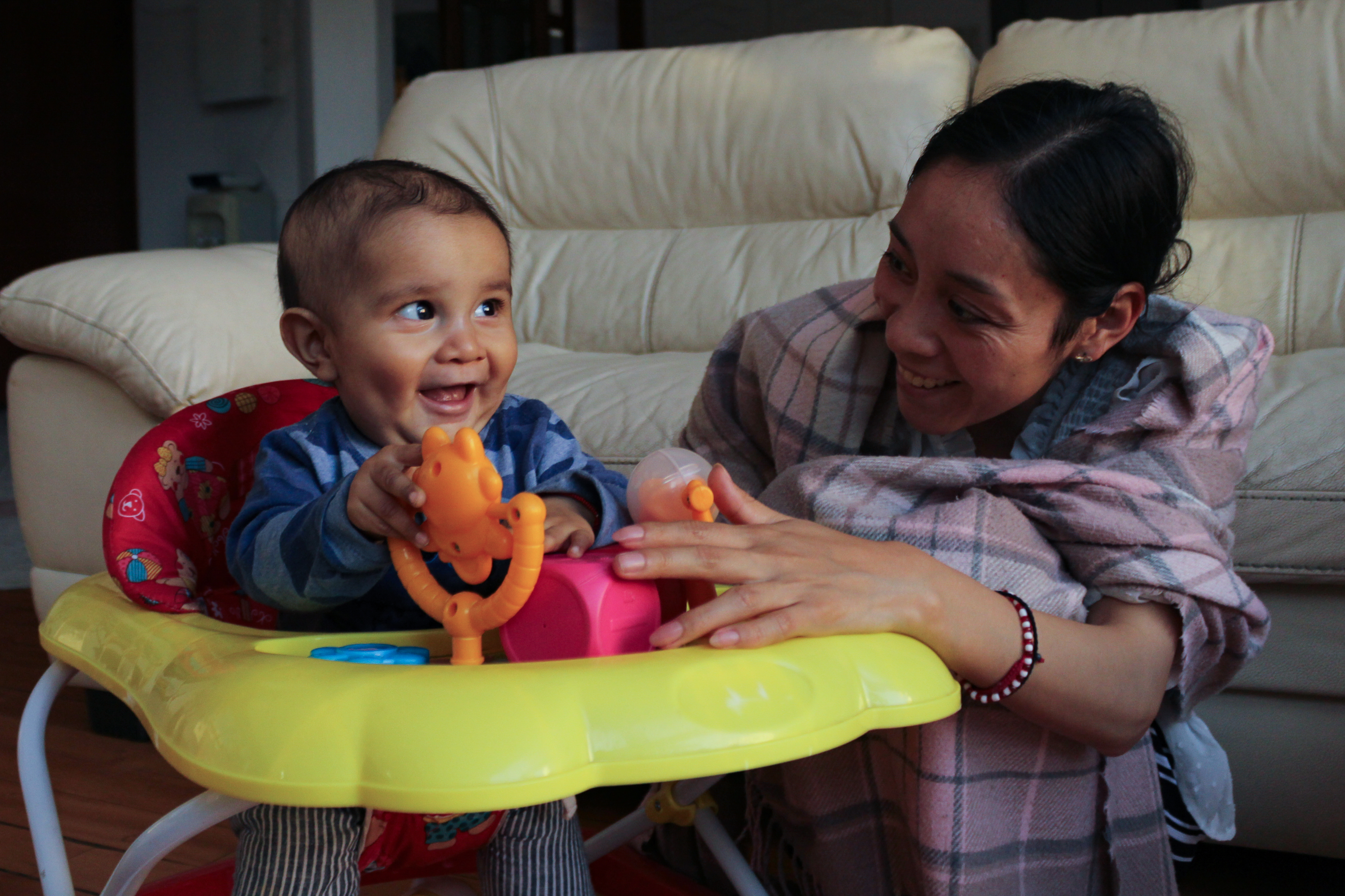 Seated in a play chair, Juan de Jesús laughs as he spins a small twirly toy, while his mother, Luisa, smiles beside him_-1773831295