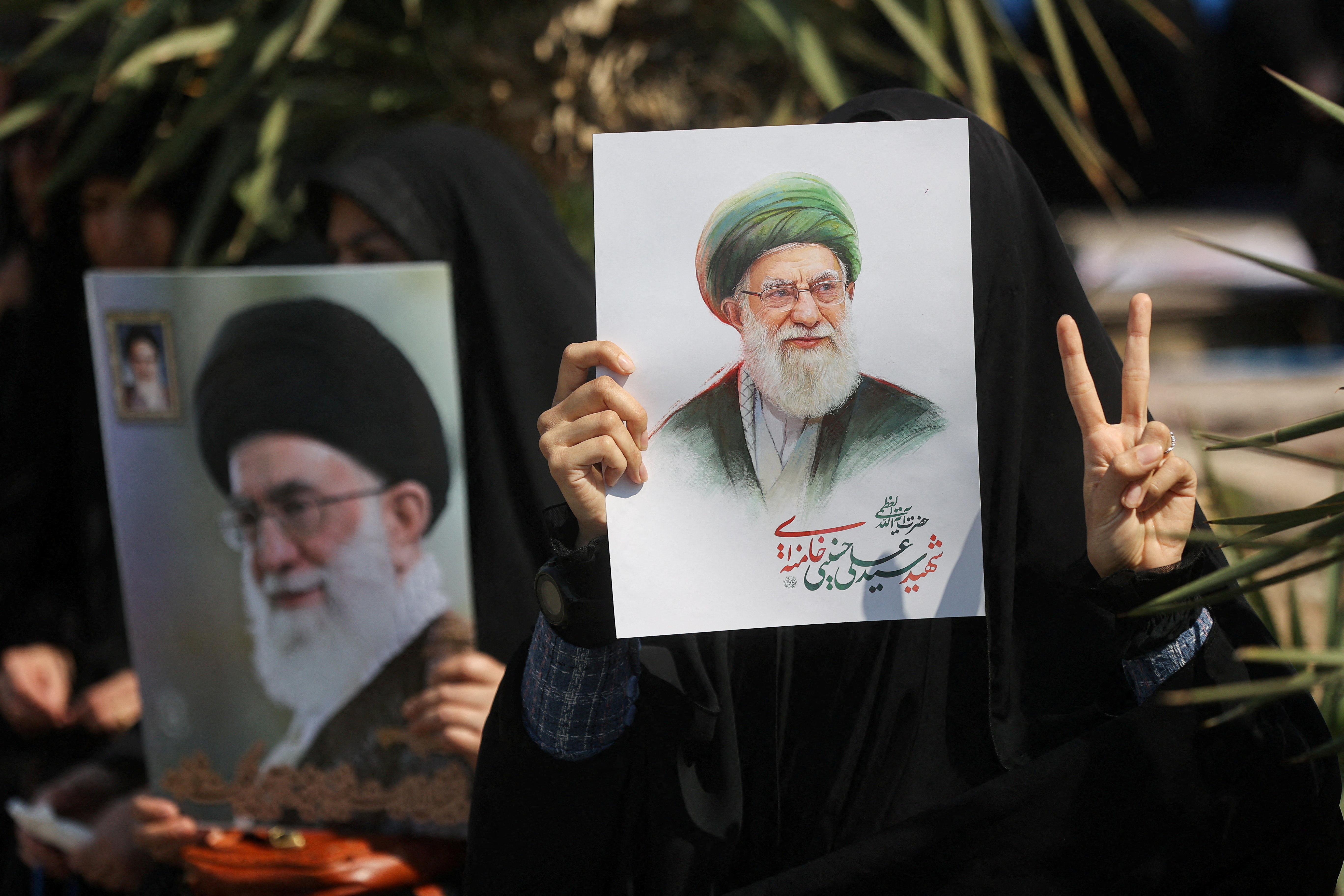 A woman gestures while holding an image of Iran's late Supreme Leader Ayatollah Ali Khamenei
