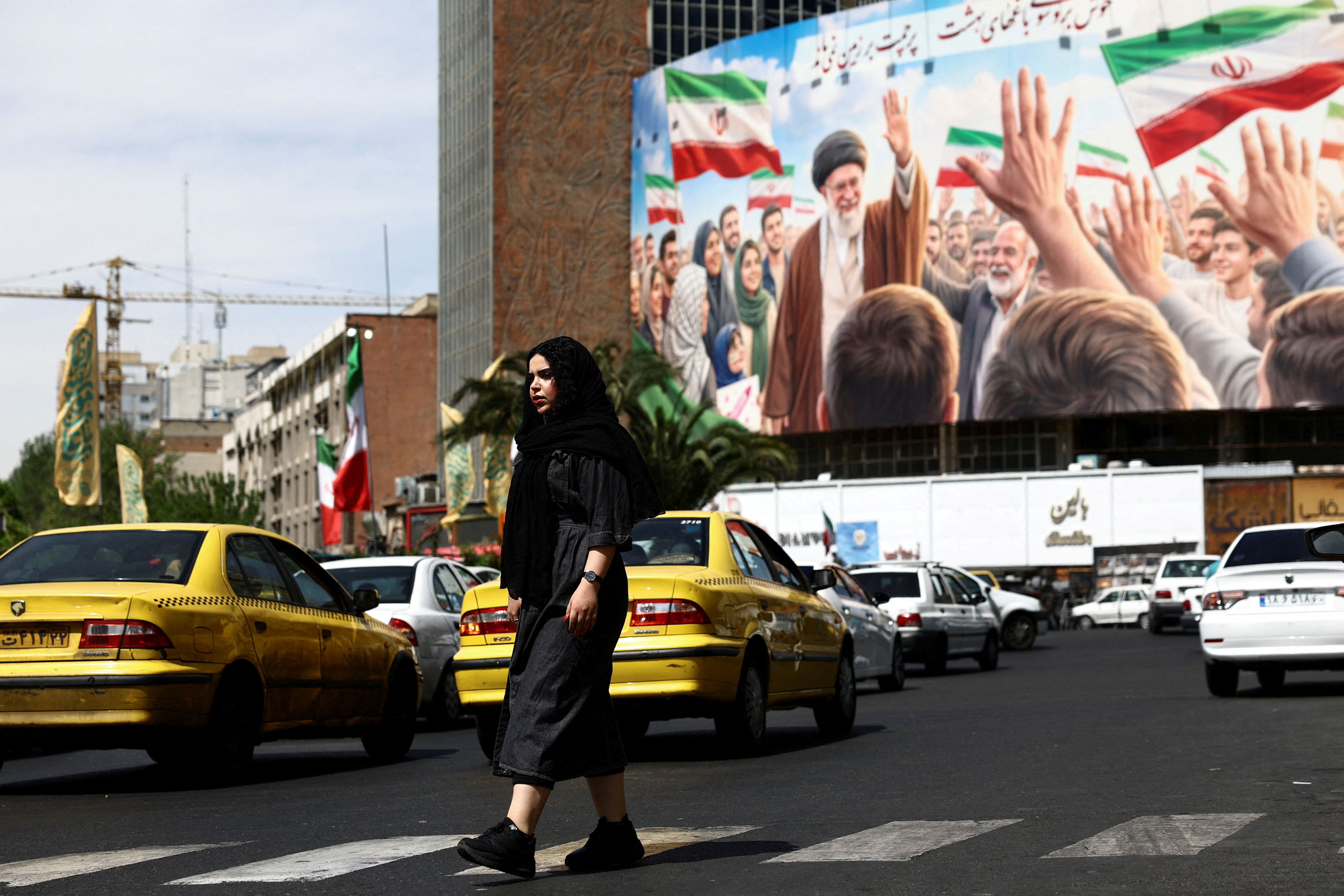 A woman walks past a billboard featuring an image of the late supreme leader of Iran, Ayatollah Ali Khamenei, on a building.