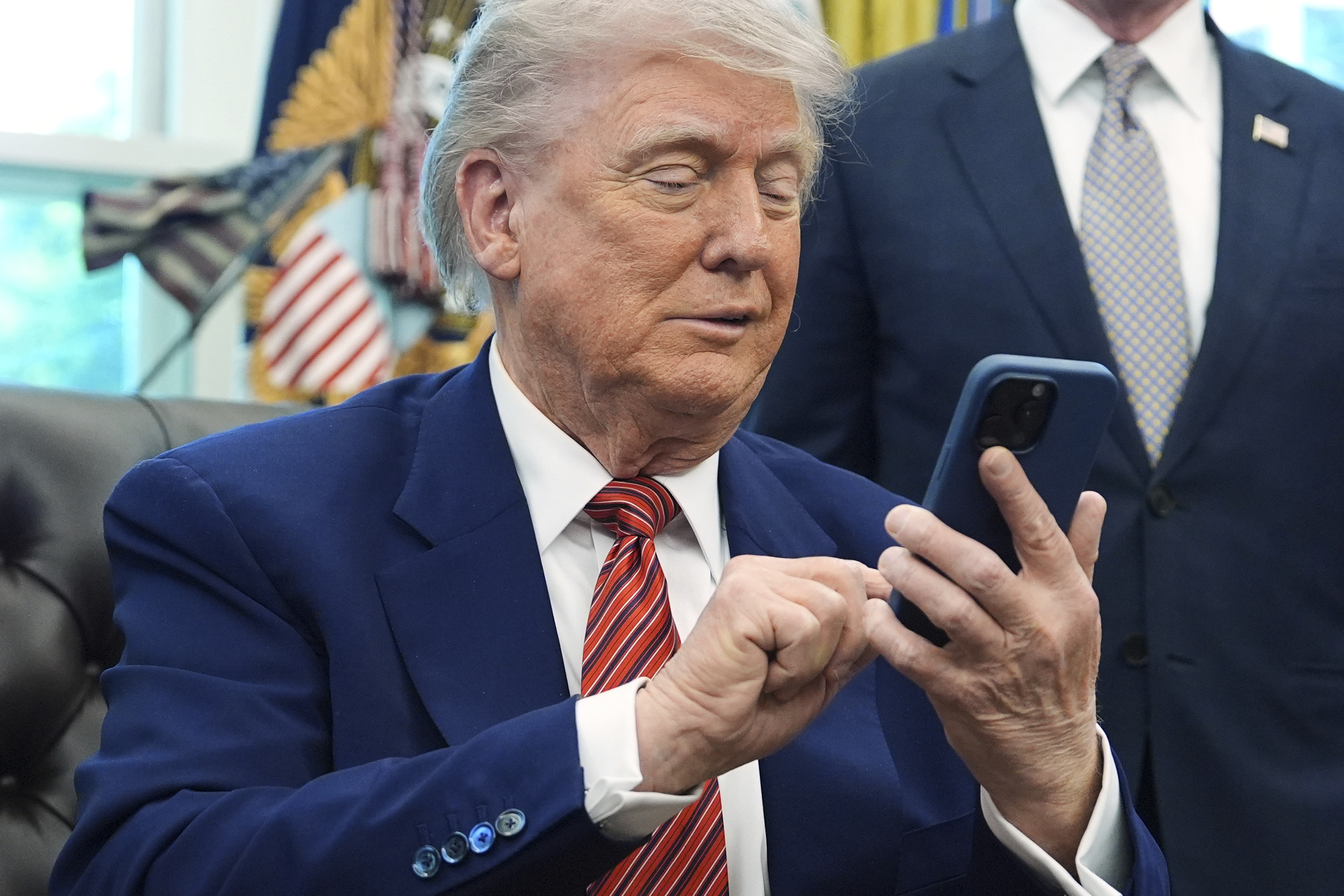 President Donald Trump silences his mobile phone which rang two times as he was speaking to reporters after signing executive orders regarding nuclear energy in the Oval Office of the White House, Friday, May 23, 2025, in Washington. (AP Photo/Evan Vucci)