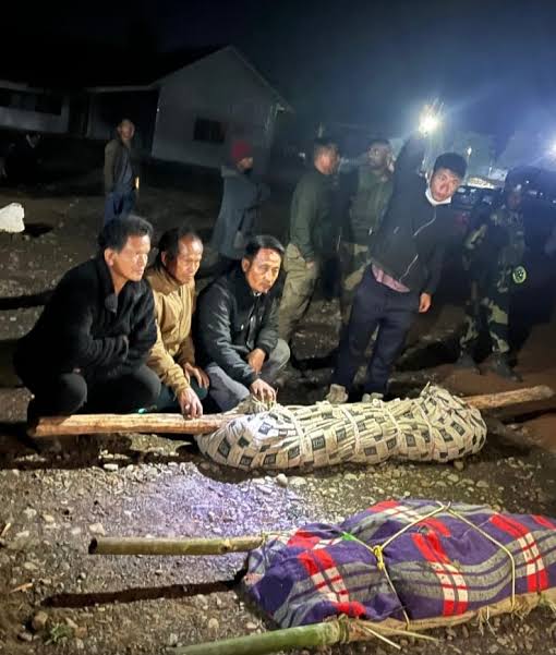 Men sit beside the bodies of two labourers killed in Ukhrul.