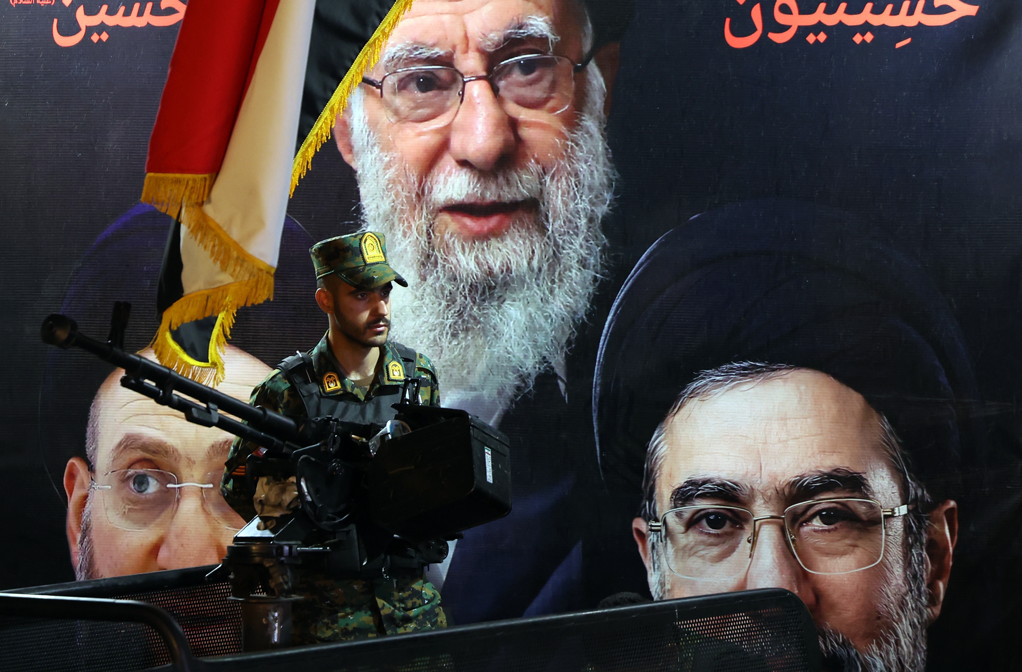 An Iranian military member stands guard in front of the picture of late Iranian Supreme Leader Ayatollah Ali Khamenei (top) and Iranian Supreme Leader Ayatollah Mojtaba Khamenei (R).