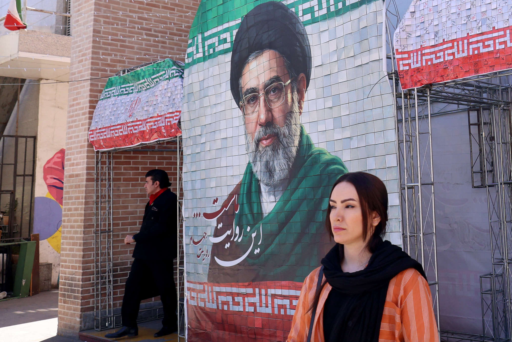 A woman walks past a large tiled image of Iran's Supreme Leader Mojtaba Khamenei in Tehran