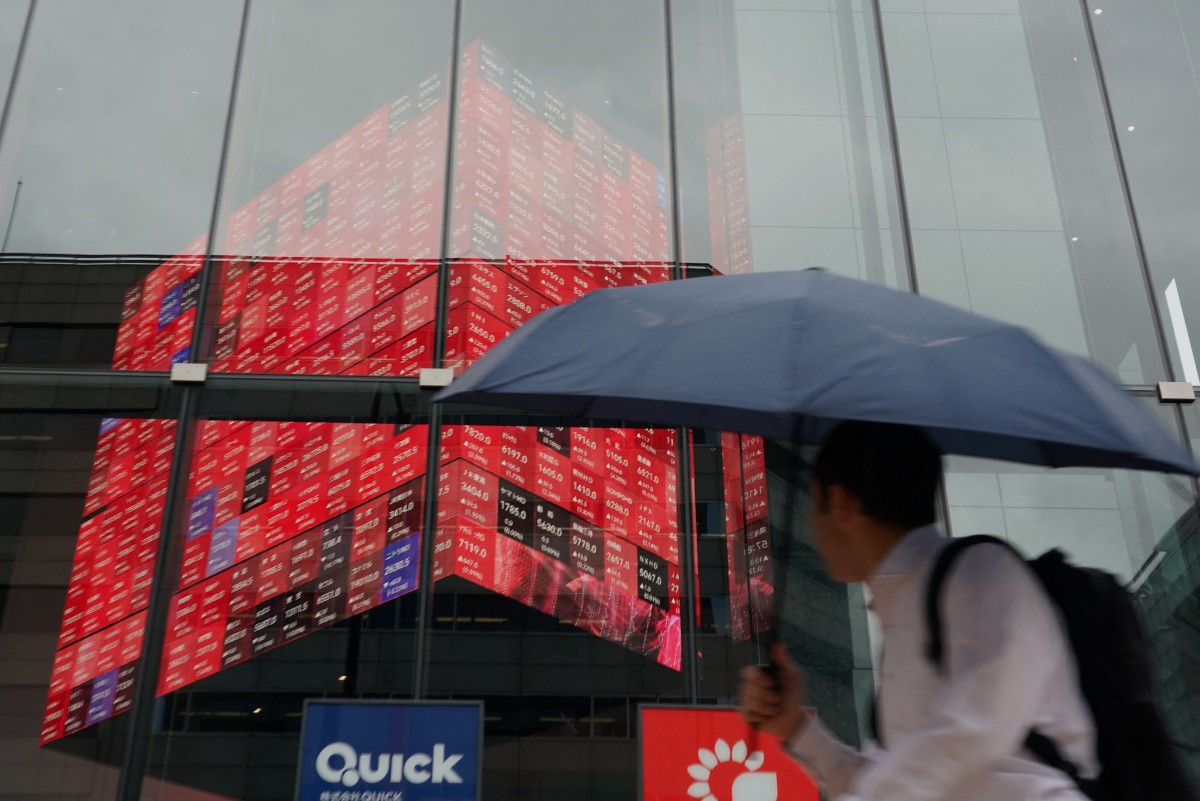 A man walks in front of an electronic quotation board displaying the Nikkei 225 stock prices on the Tokyo Stock Exchange in Tokyo [File: Kazuhiro Nogi/AFP]