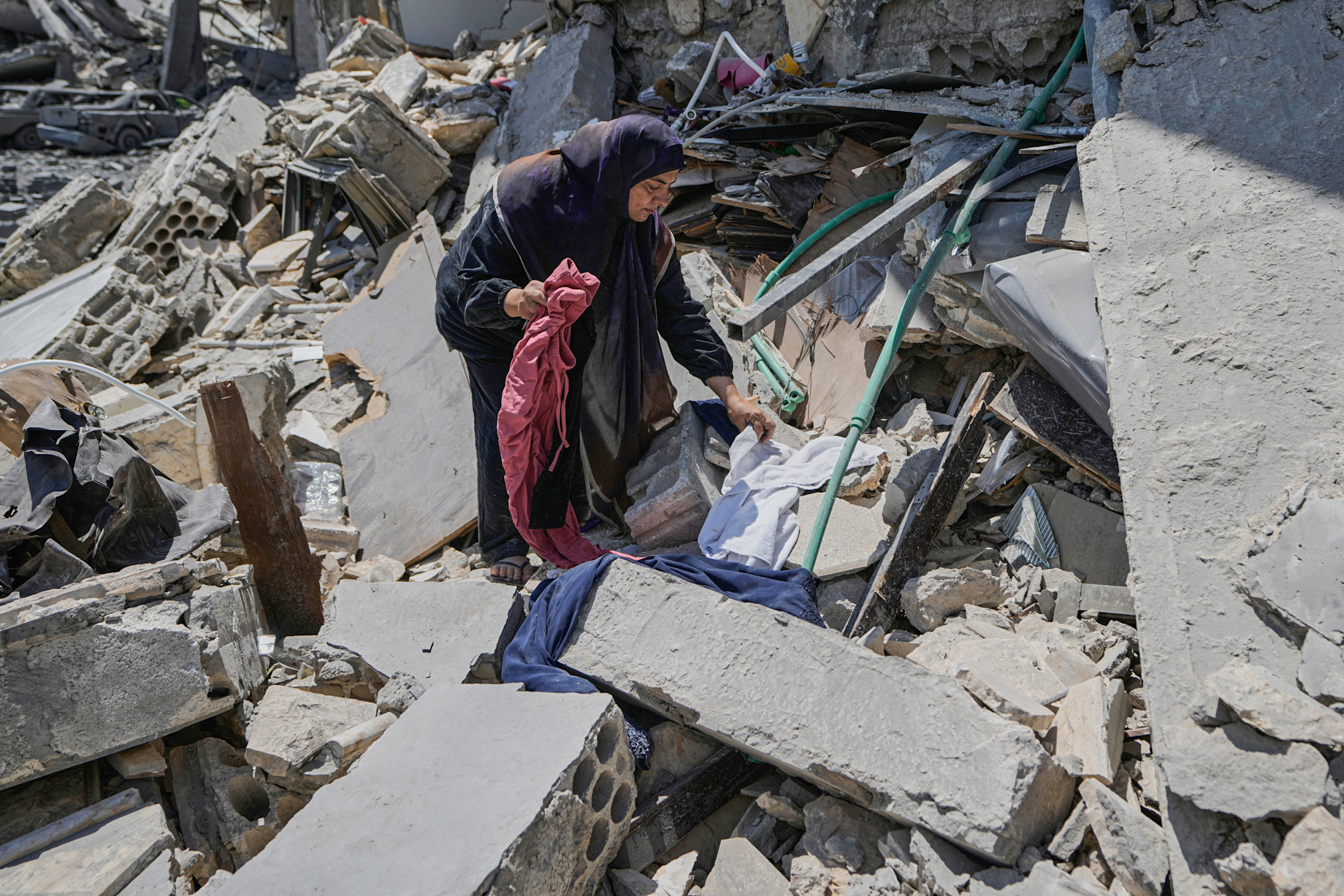 A woman collects belongings from the rubble of a home.