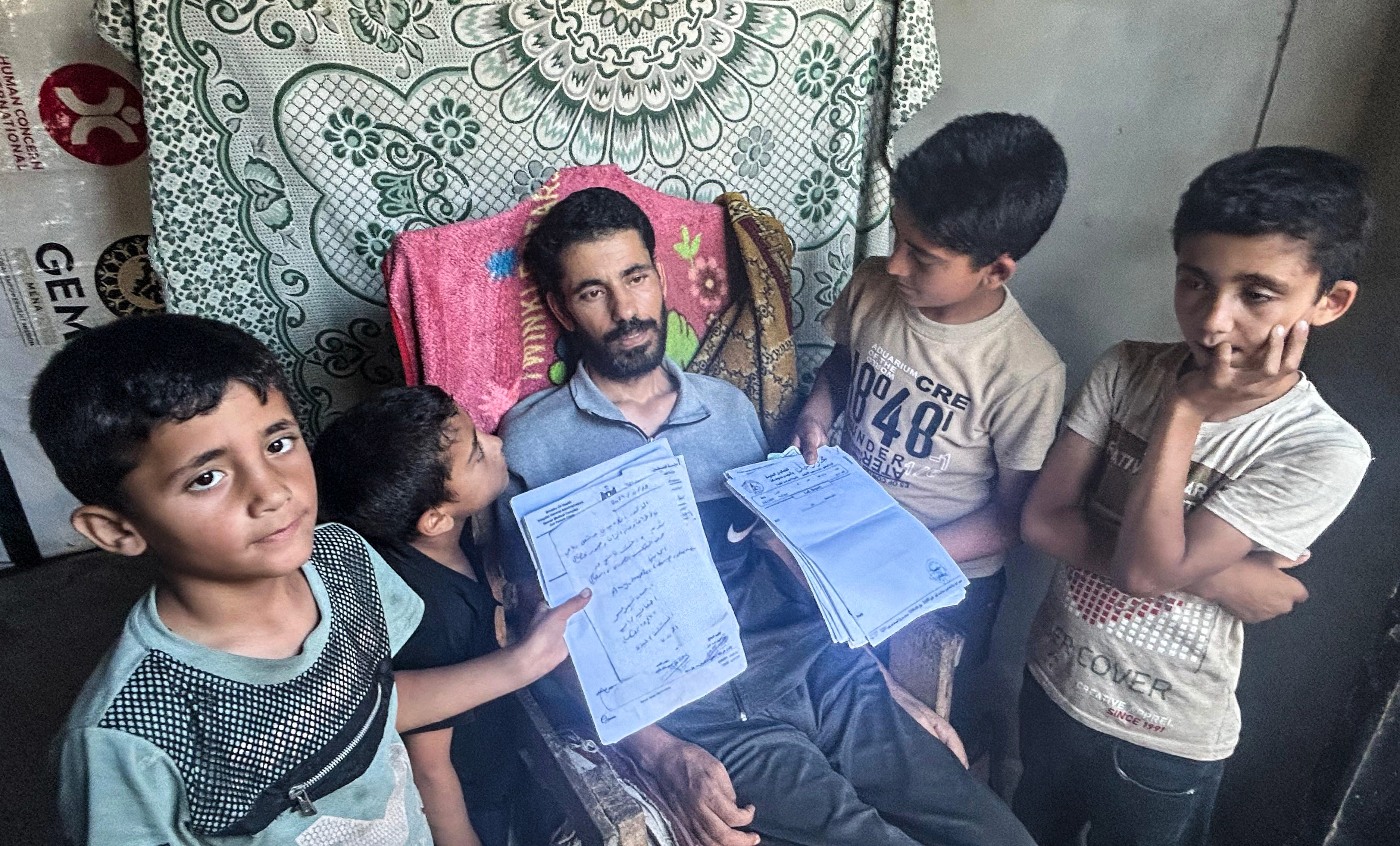 Ismail al-Aqqad with his four children in al-Mawasi, Gaza, displaying his medical papers