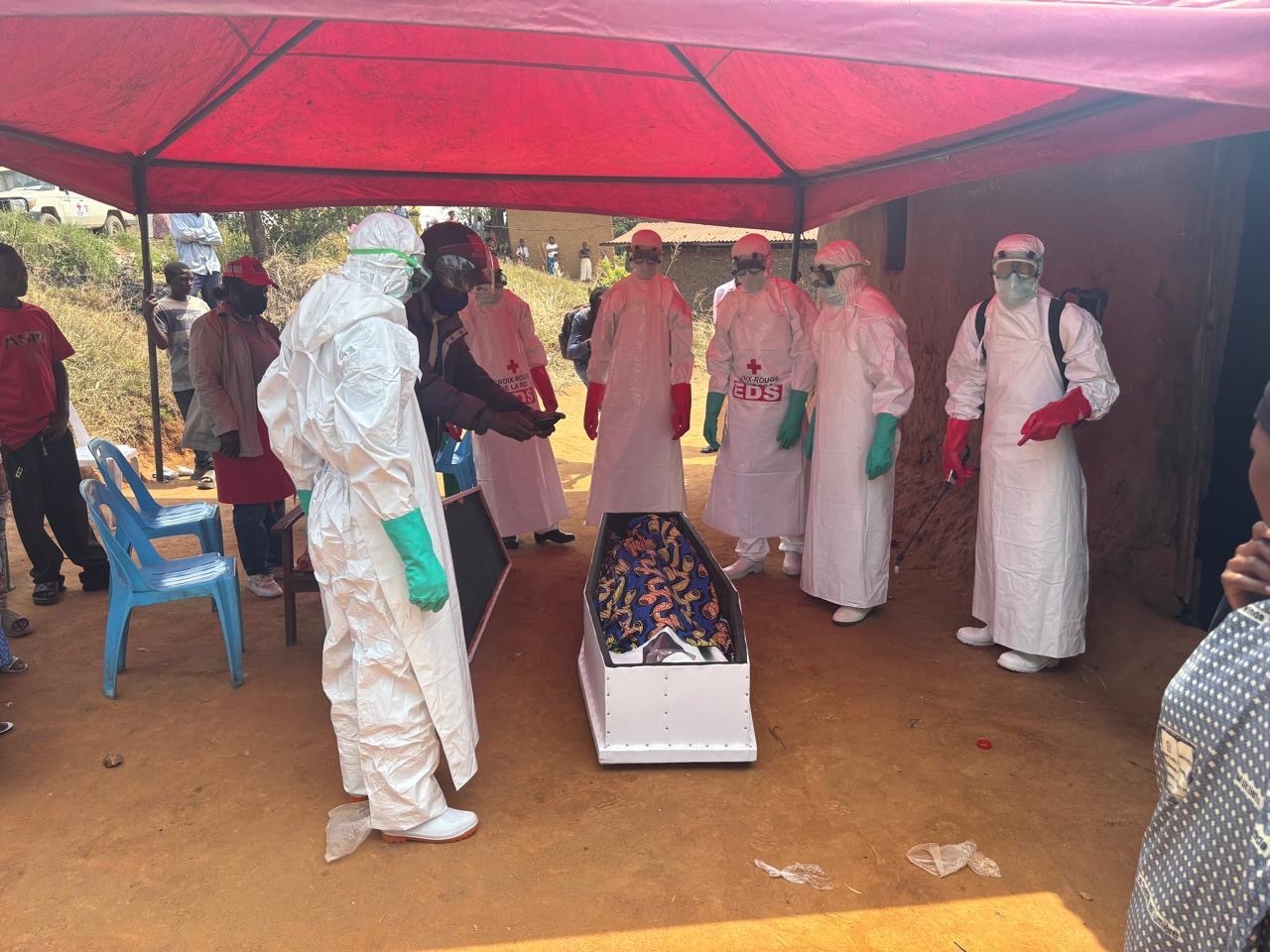 A burial team in full protective gear prepares a coffin.